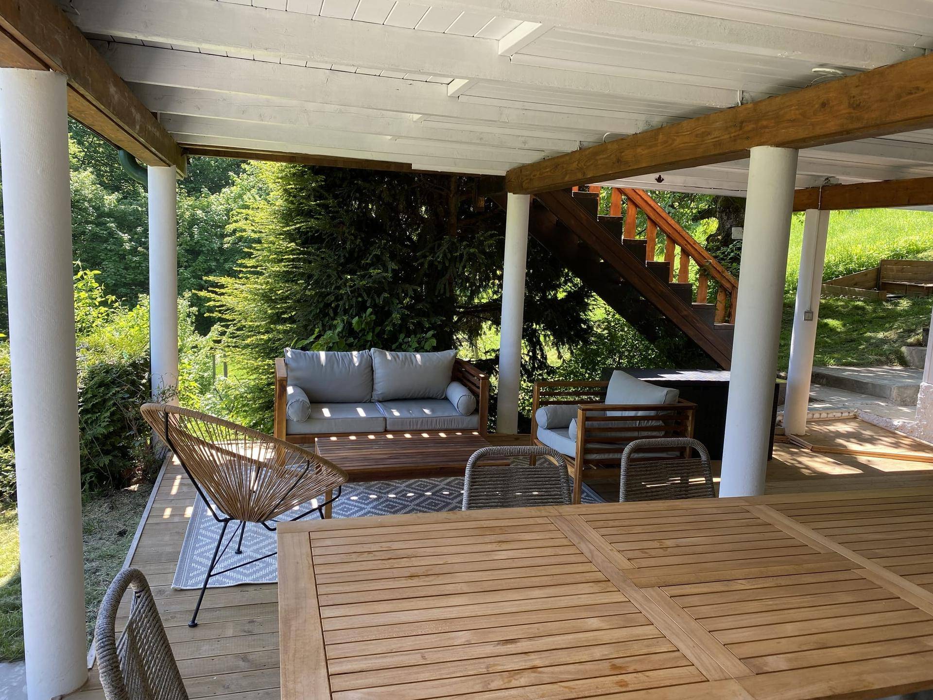 Überdachte Terrasse mit bequemen Lounge-Möbeln und Esstisch im Grünen.