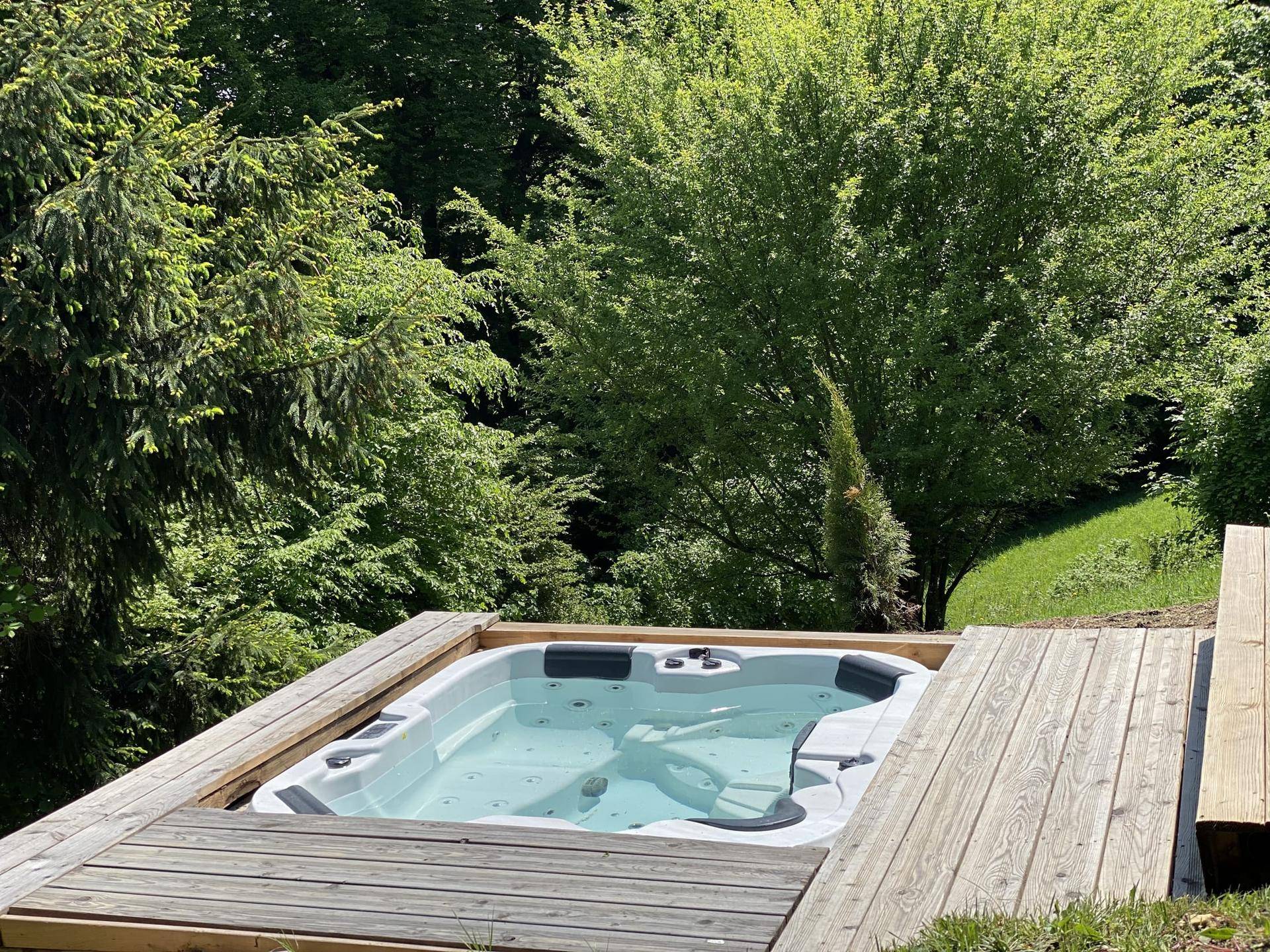 Integrierter Whirlpool auf einer Holzterrasse, umgeben von Bäumen und Natur.