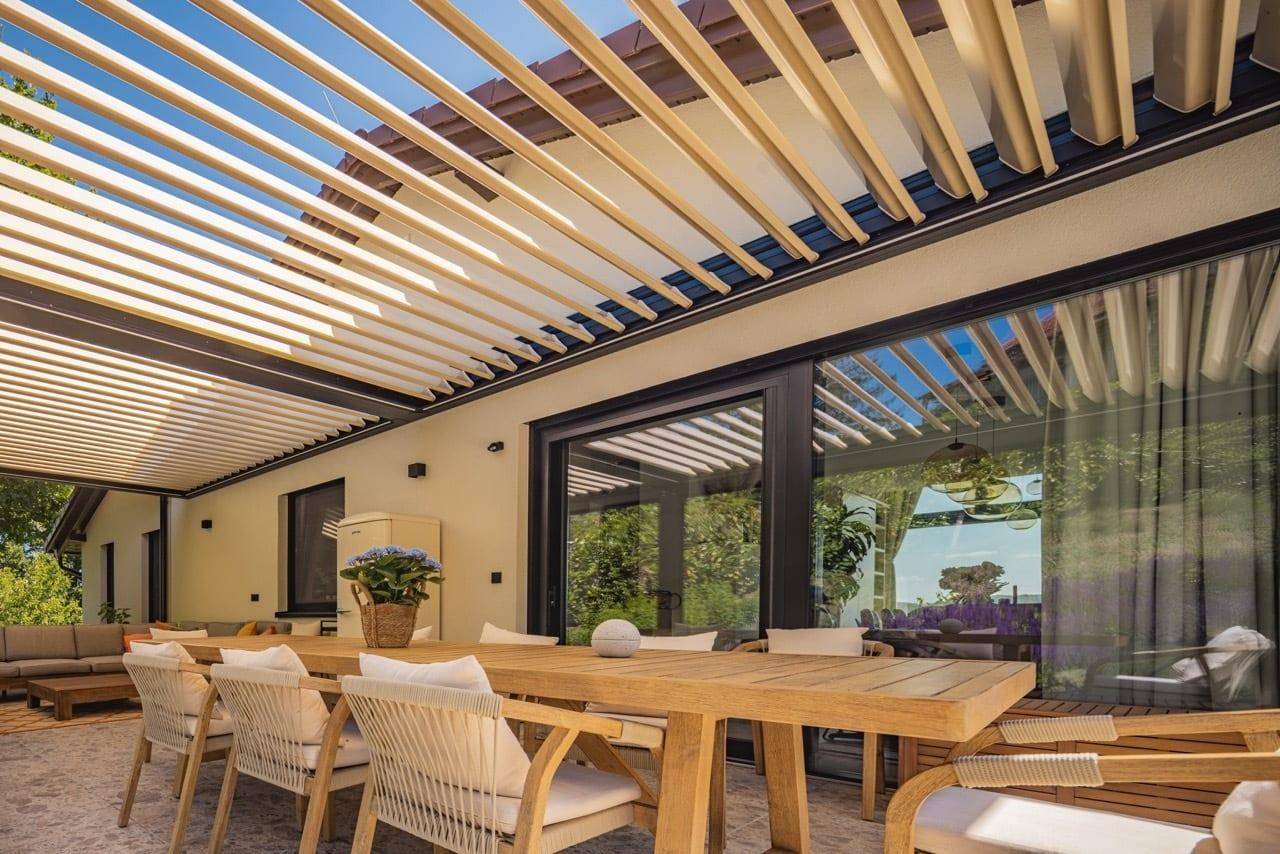 Elegante überdachte Terrasse mit Lamellen-Pergola und großen Schiebetüren zum Innenbereich.