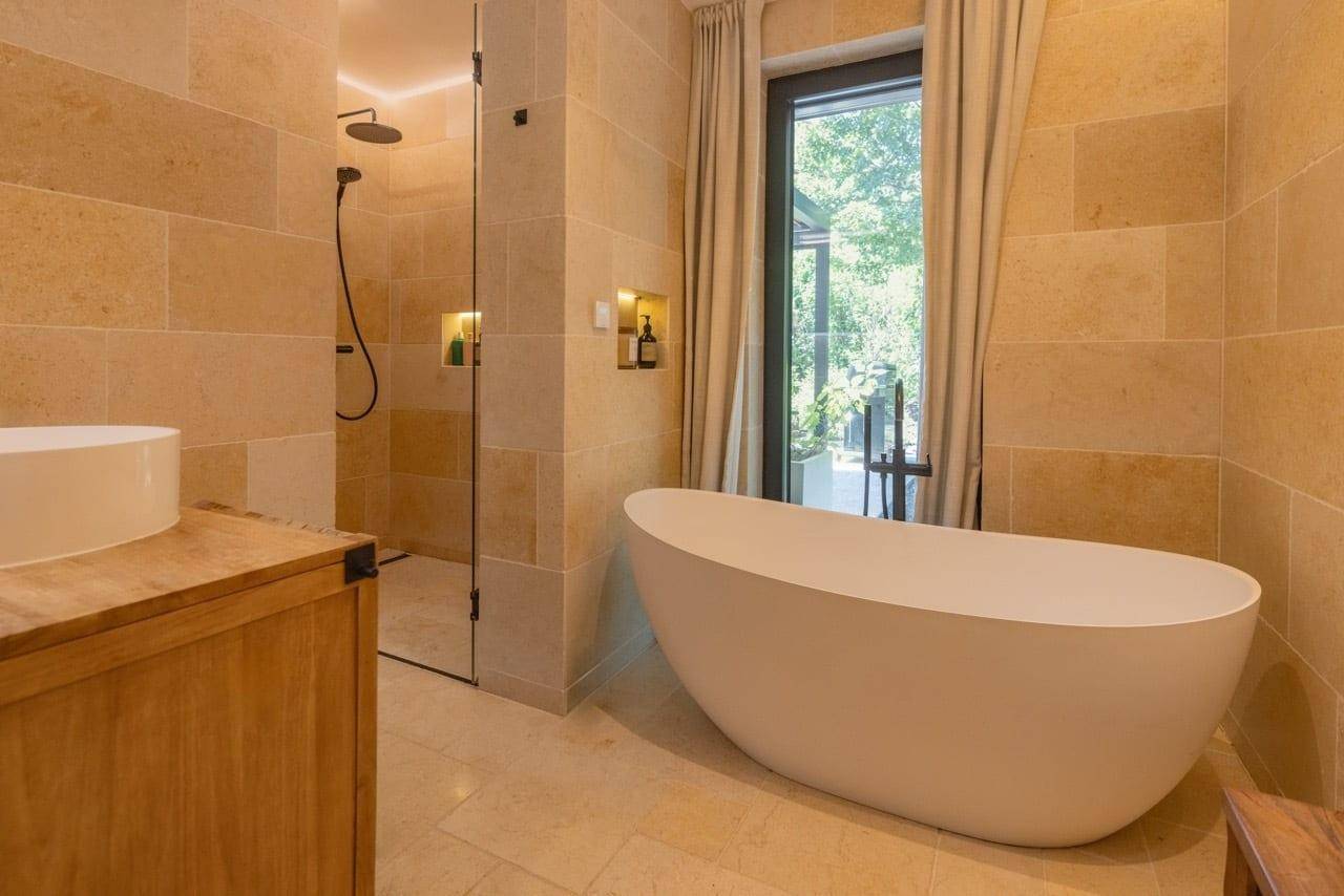 Luxuriöses Badezimmer mit freistehender Badewanne, begehbarer Dusche und Natursteinfliesen.
