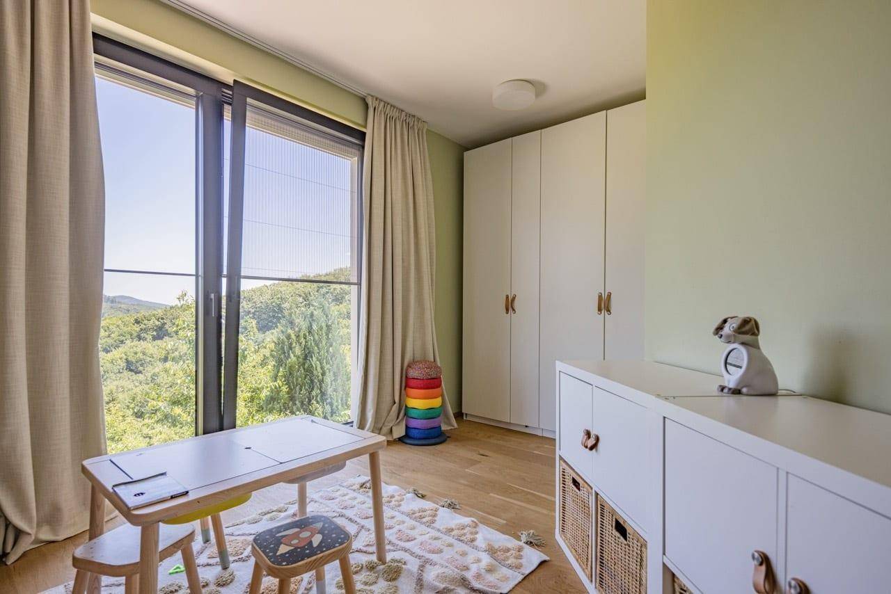 Helles Kinderzimmer mit großen Fenstern, Holzboden und Blick ins Grüne.