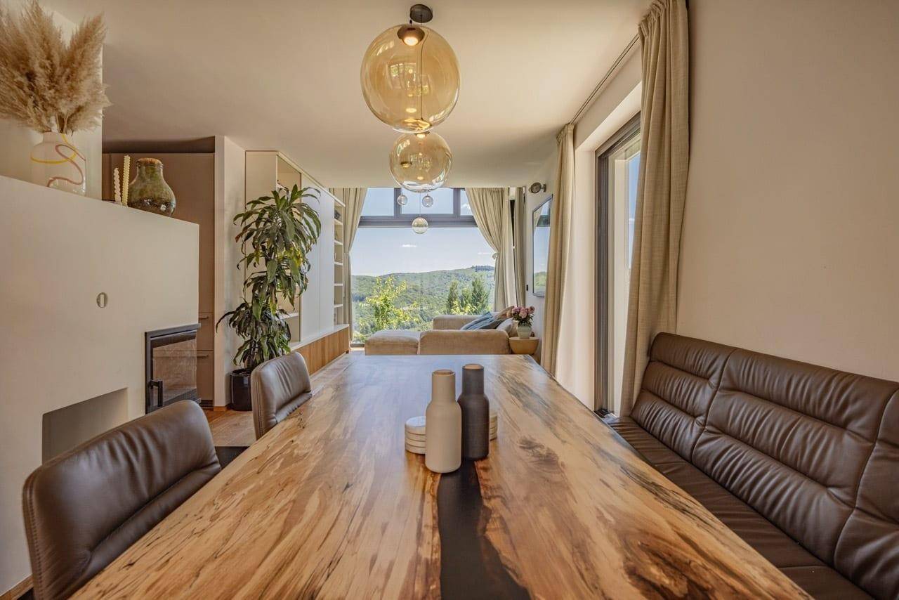 Eleganter Essbereich mit großem Holztisch, Lederbank und Panoramafenstern mit weitem Ausblick.