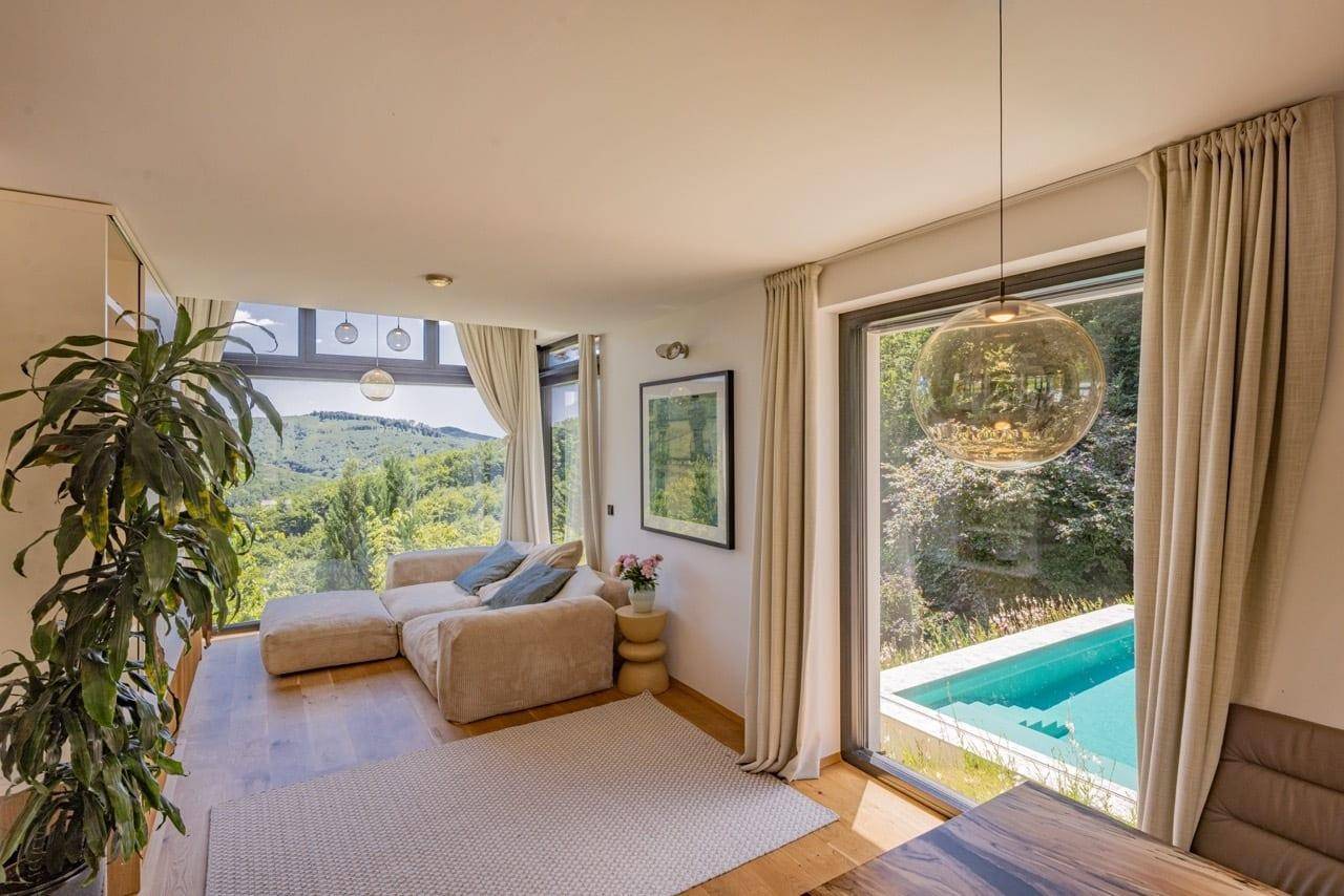 Helles Wohnzimmer mit bequemer Couch, großen Fenstern und direktem Blick auf den Pool und die Landschaft.