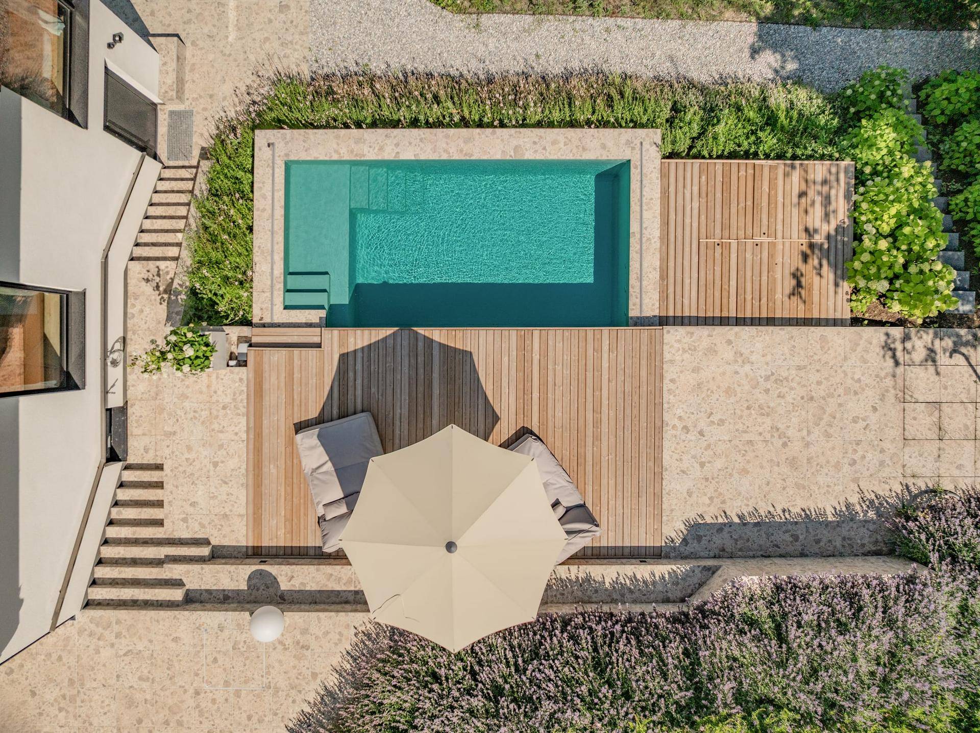Vogelperspektive des Außenbereichs mit modernem Pool, Holzdeck und Liegeflächen unter einem Sonnenschirm.