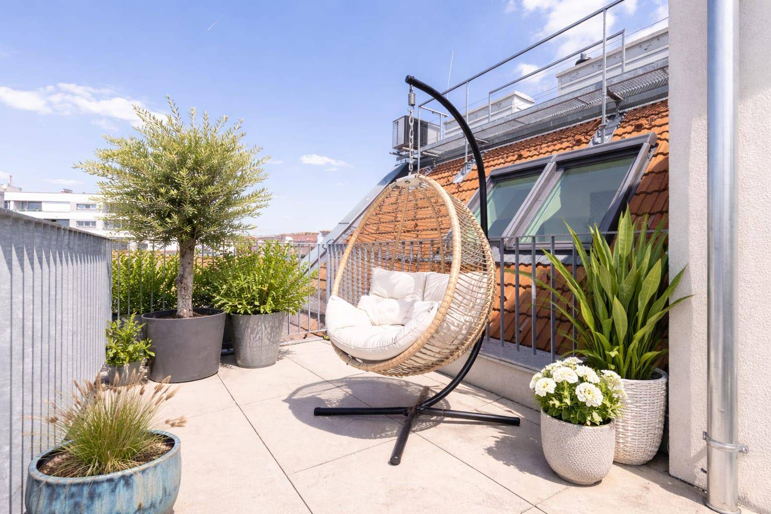 Sonniger Terrassenbereich mit Hängesessel, Pflanzen und Blick auf die Dächer.
