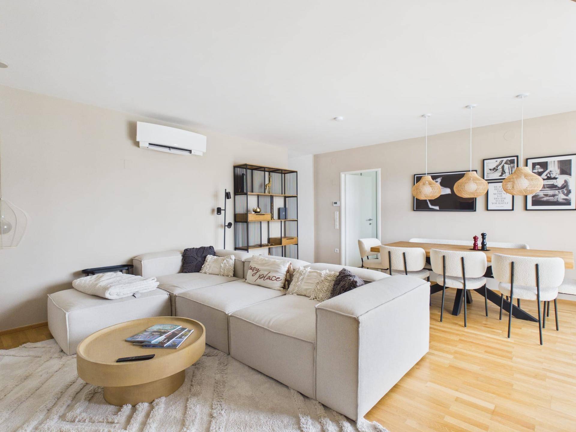 Heller Wohn- und Essbereich mit modernem Sofa, Holzboden und Klimaanlage für angenehmes Raumklima.