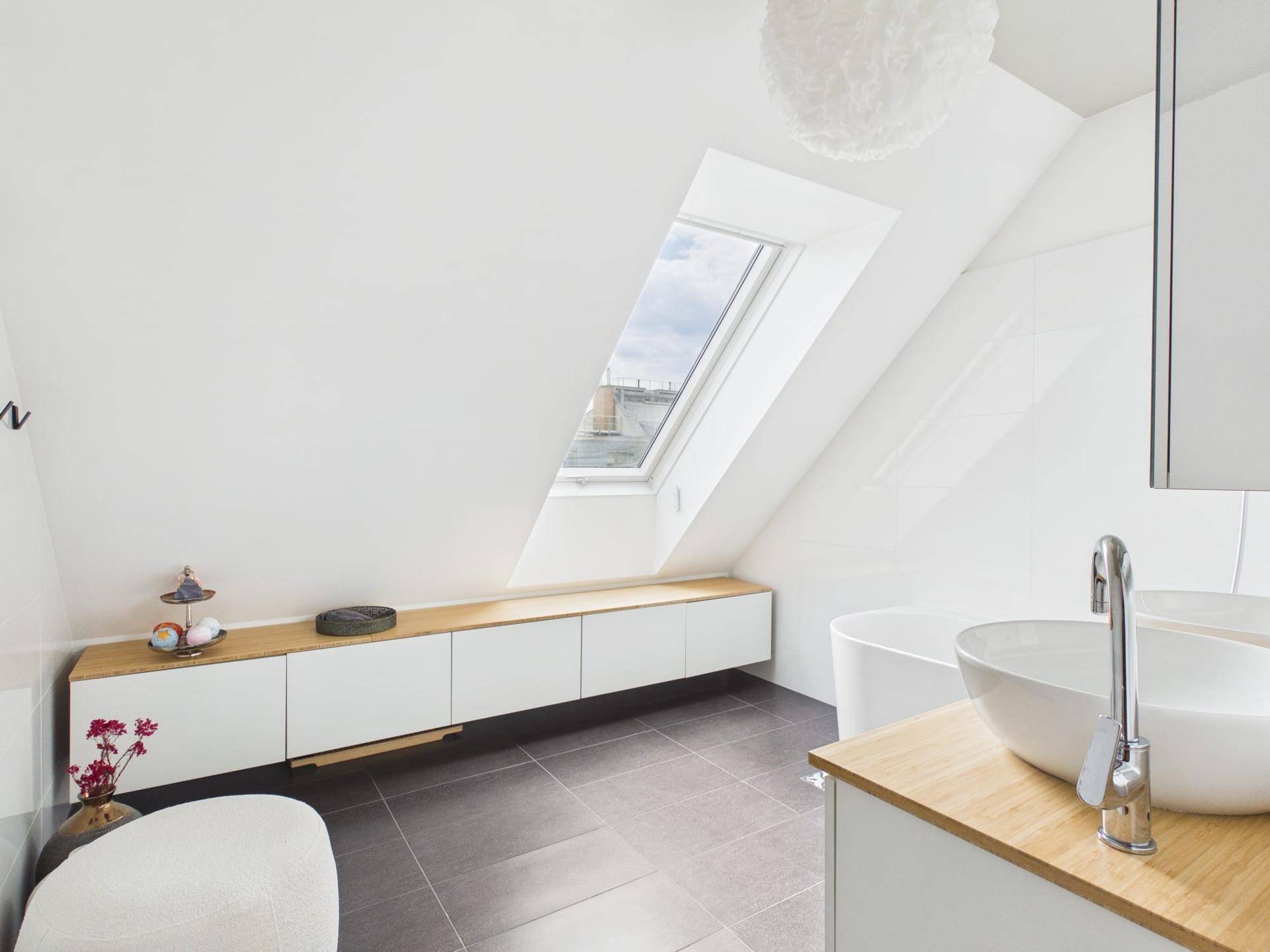 Modernes Badezimmer im Dachgeschoss mit schräger Decke, freistehender Badewanne und einem Dachfenster für natürliches Licht.