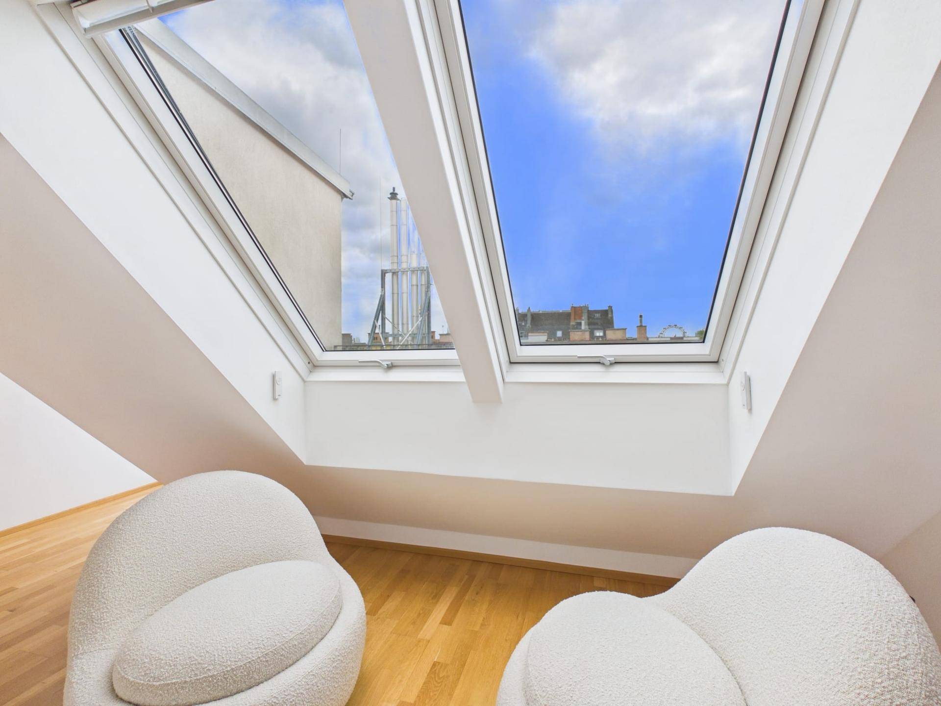 Nahaufnahme der Dachfenster im Dachgeschoss, die einen weiten Blick auf den Himmel und die umliegenden Gebäude bieten.