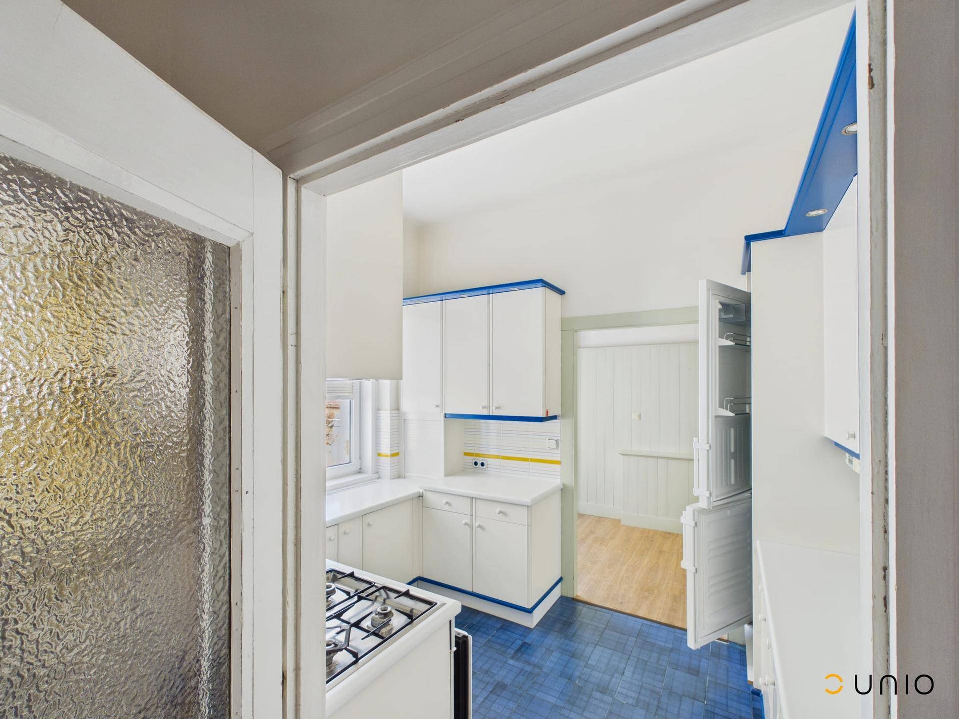 Küche mit blauen Fliesen und weißen Schränken, die einen Gasherd und einen Kühlschrank umfasst.