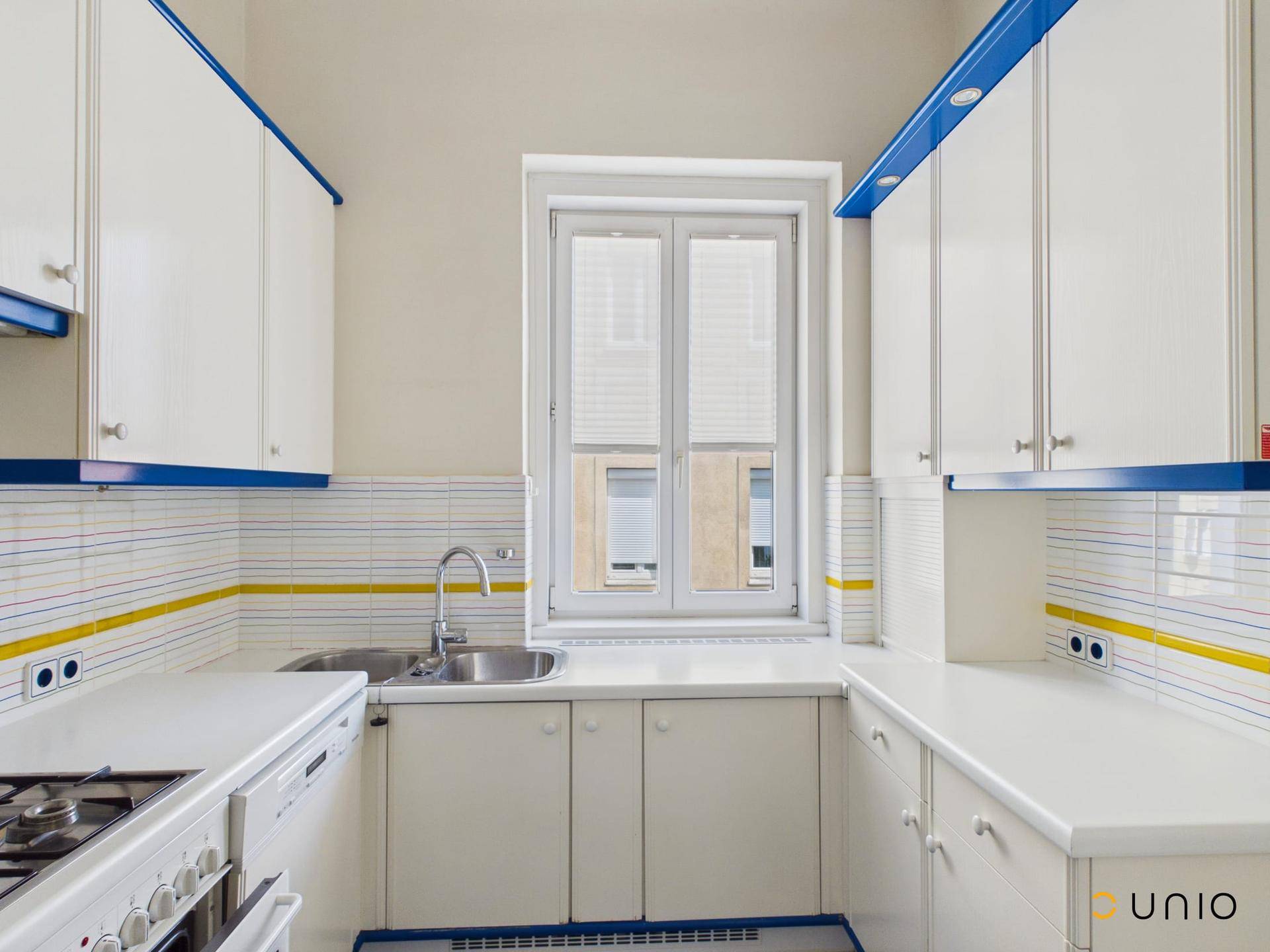 Helle Küche mit weißen Schränken, blauen Akzenten und einem Fenster über der Spüle.