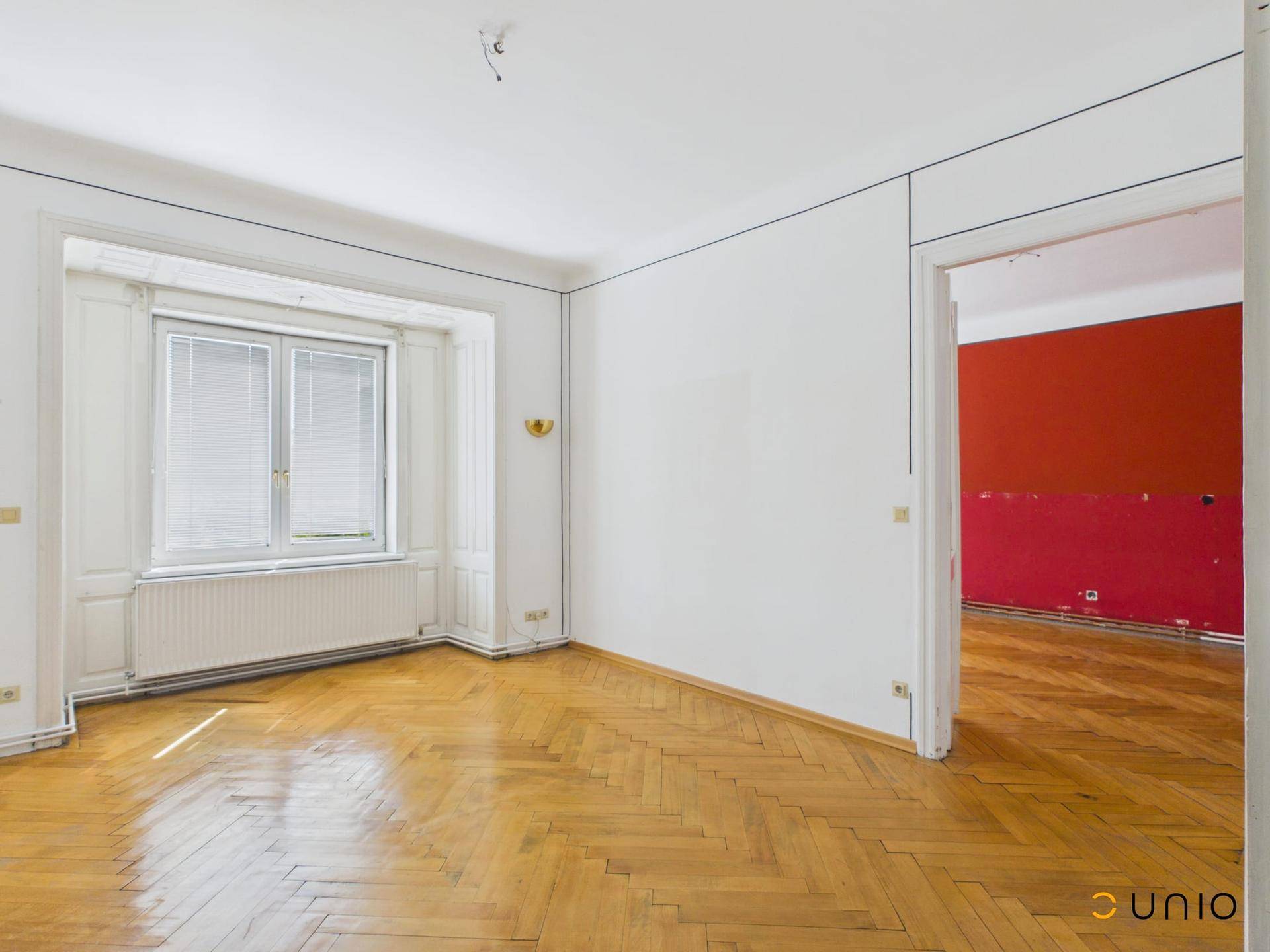 Geräumiges Wohnzimmer mit Fischgrätparkett und einem Erkerfenster, bereit zur Renovierung.