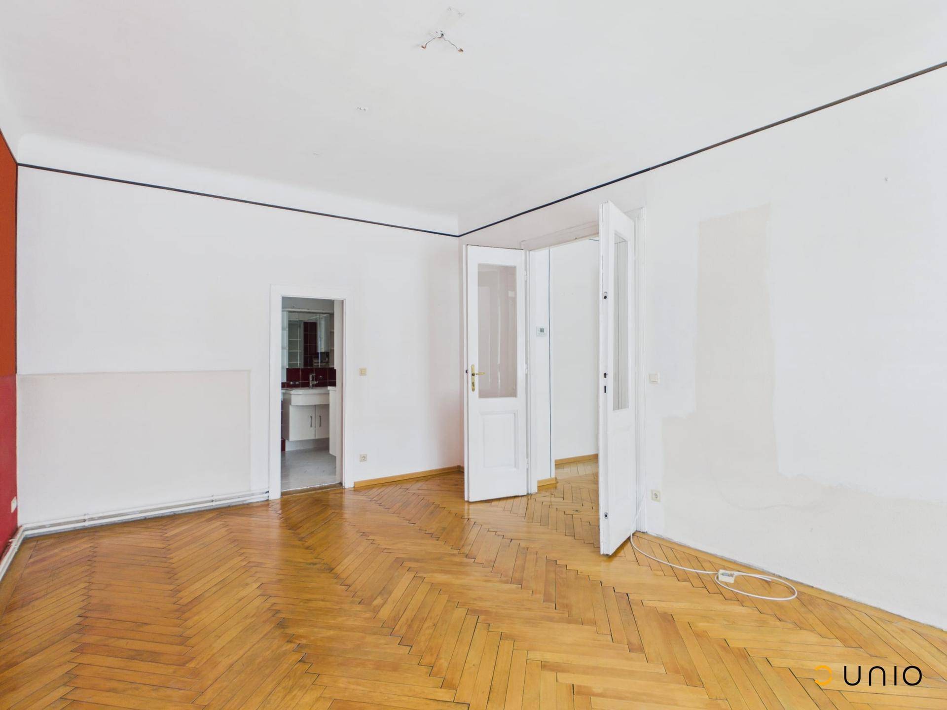 Geräumiges Zimmer mit Fischgrätparkett und Zugang zu einem Badezimmer.