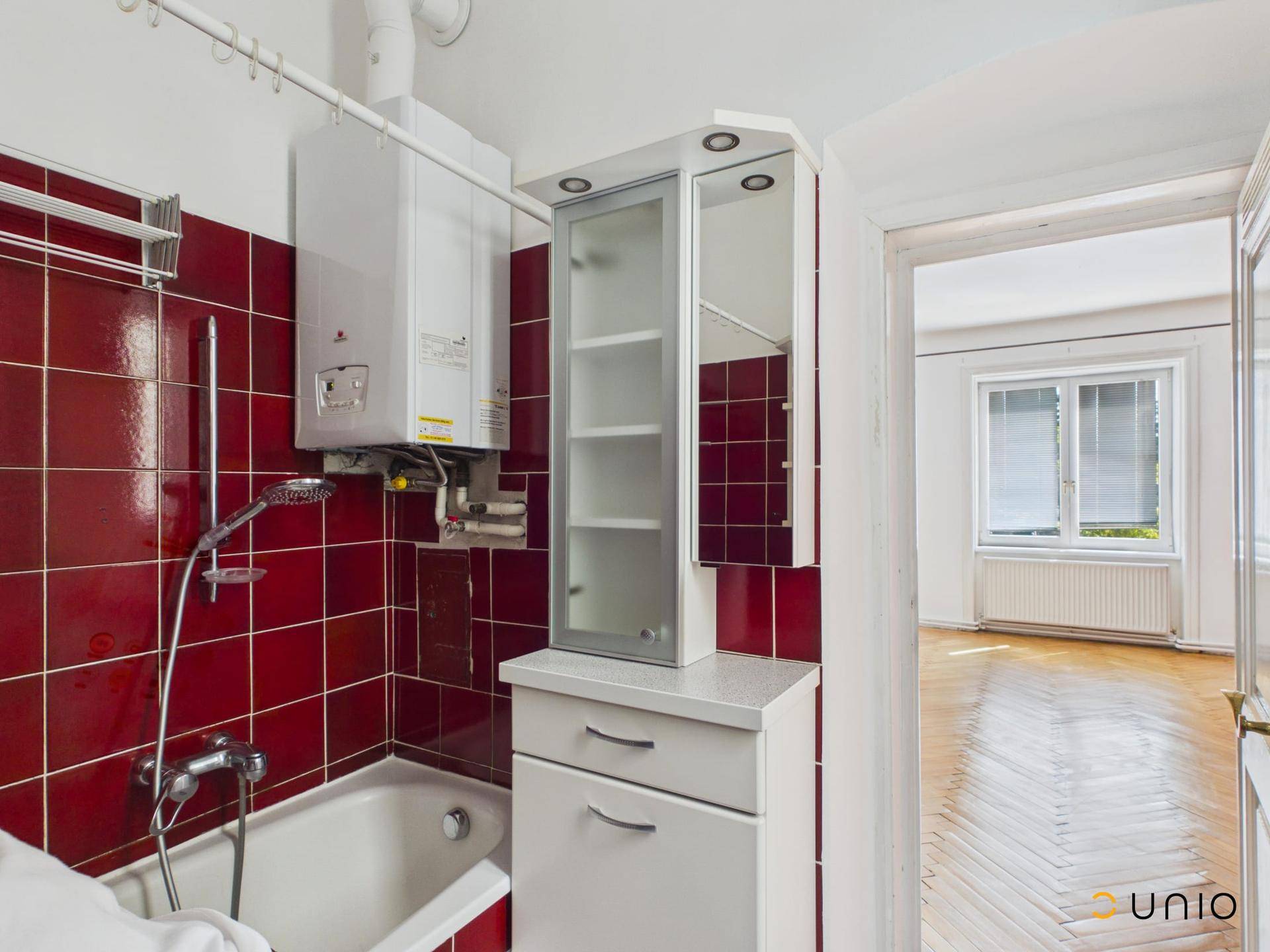 Badezimmer mit roten Fliesen, Badewanne und Gastherme, angrenzend an ein Zimmer.