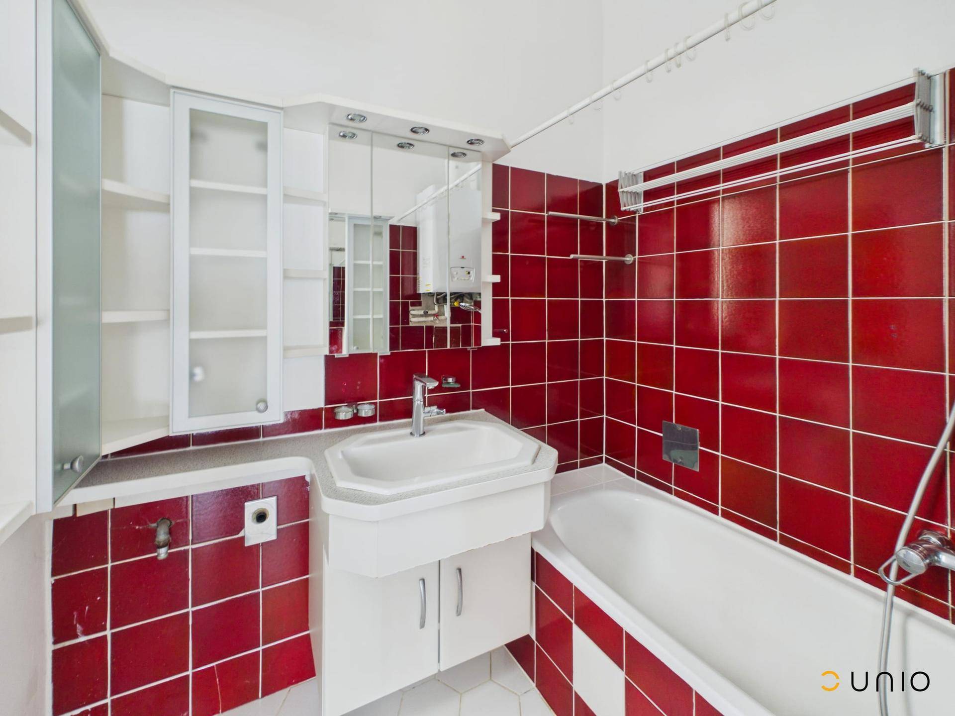 Badezimmer mit roten Wandfliesen, Badewanne und Waschbecken mit Spiegelschrank.