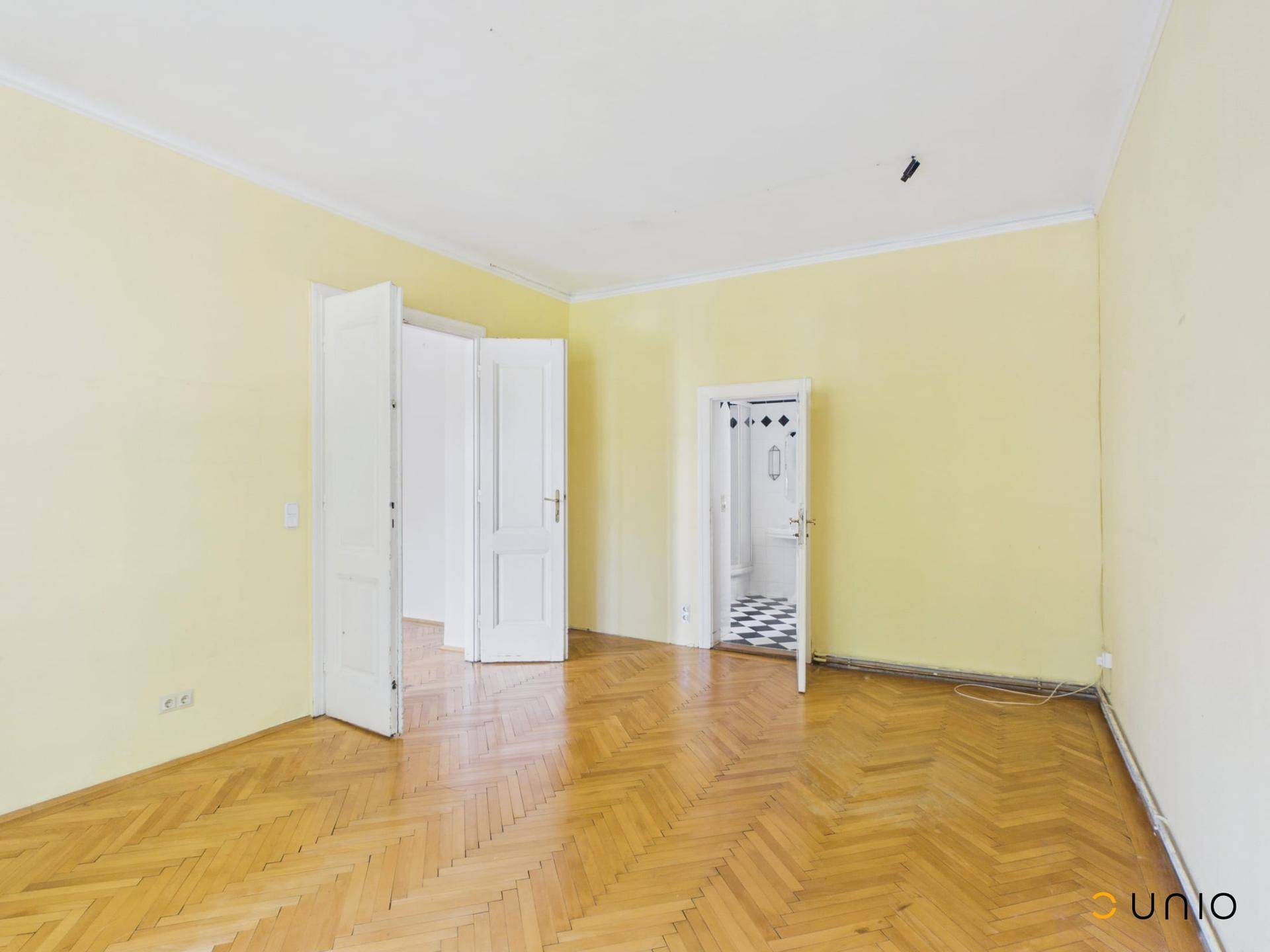 Helles Zimmer mit gelben Wänden und Fischgrätparkett, mit Zugang zu einem Badezimmer.