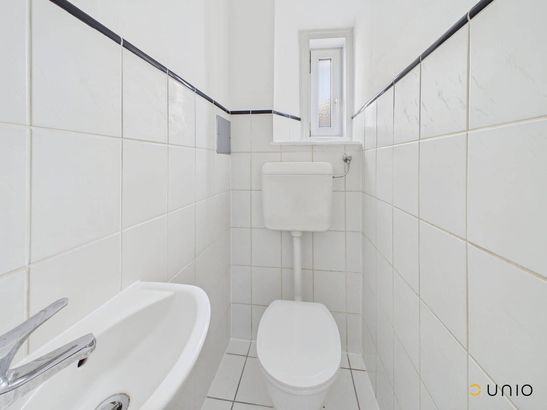 Kleines Gäste-WC mit Fenster, weiß gefliesten Wänden und klassischer Toilette.