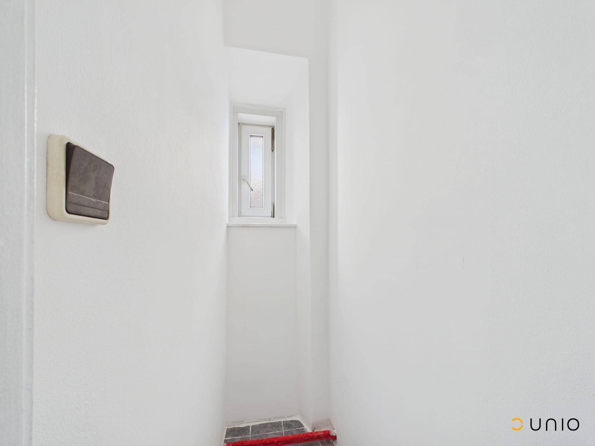 Kleiner Raum mit Fenster und weißen Wänden, möglicherweise ein Abstellraum.