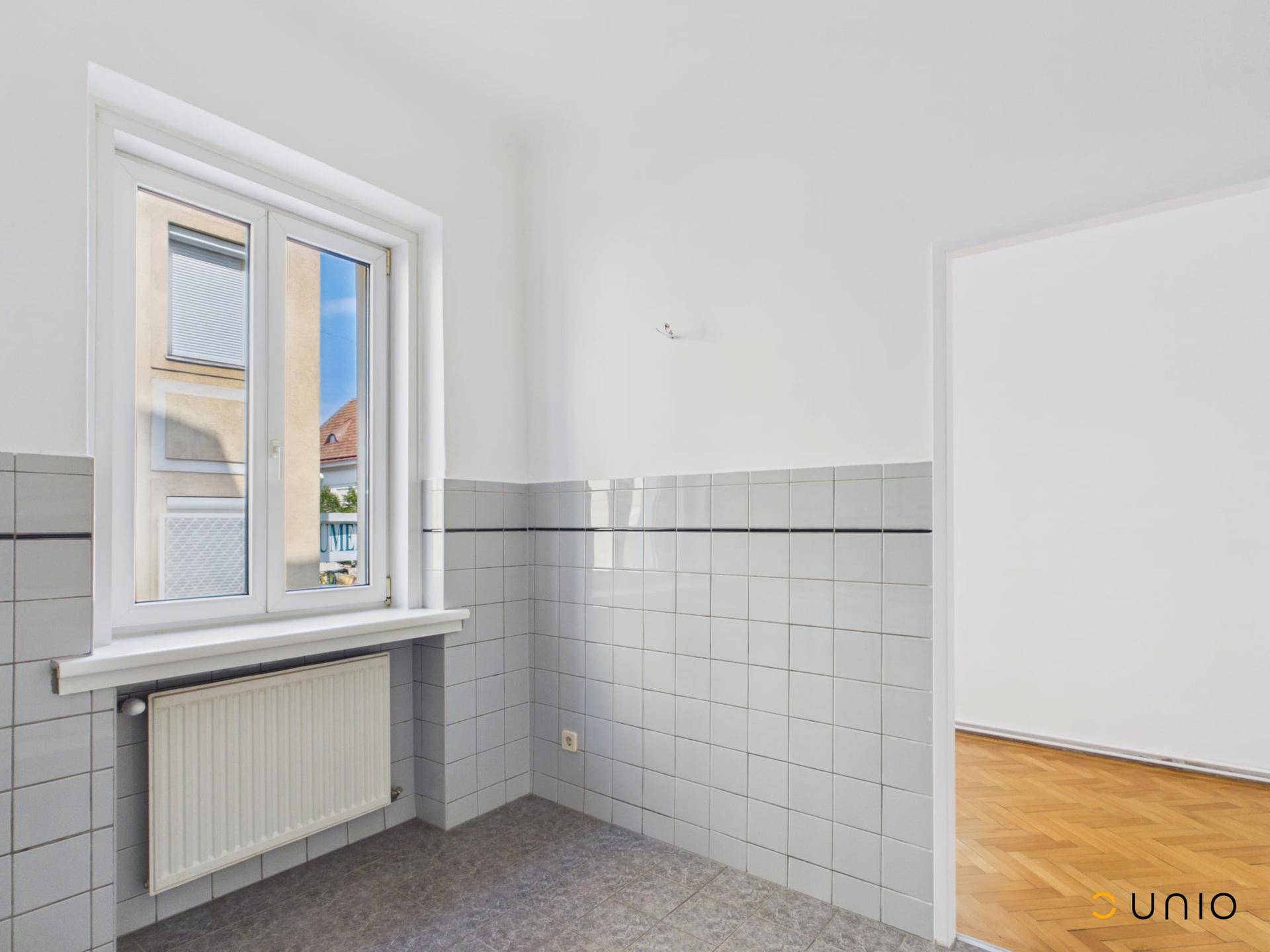 Raum mit gefliesten Wänden und Fenster, vorbereitet für eine Kücheninstallation.