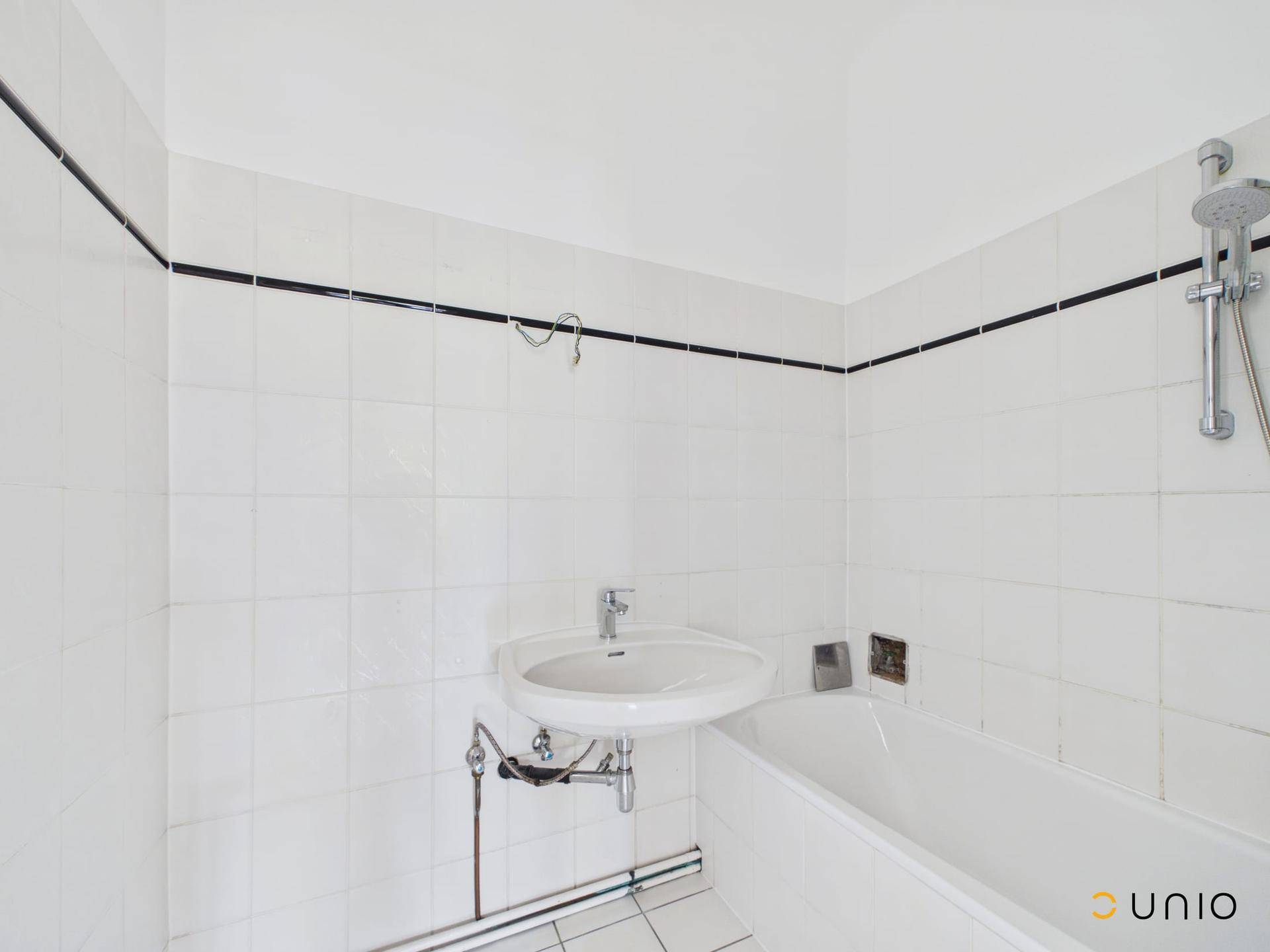Badezimmer mit Badewanne, Waschbecken und weißen Fliesen, bereit zur Modernisierung.