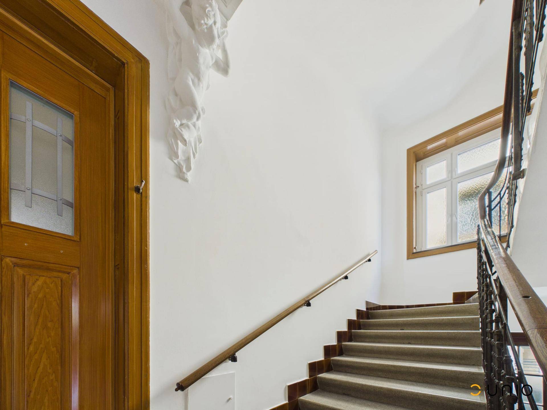 Historisches Treppenhaus mit Stuckelementen, Holzgeländer und Fenster, zeugt von Altbaucharme.