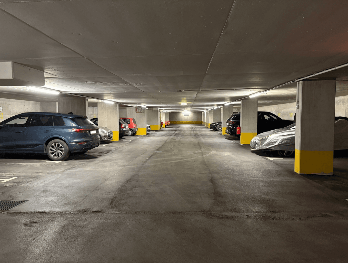 Helle Tiefgarage mit vielen Parkplätzen, Betonpfeilern und guter Beleuchtung für Fahrzeuge.