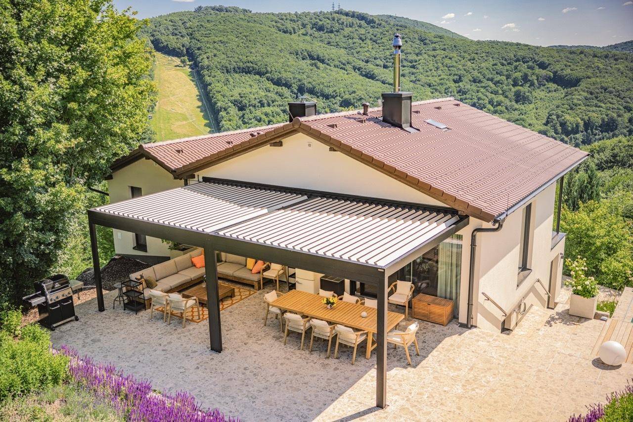 Großzügige Terrasse mit Pergola, Essbereich und Lounge-Möbeln, umgeben von grüner Landschaft.