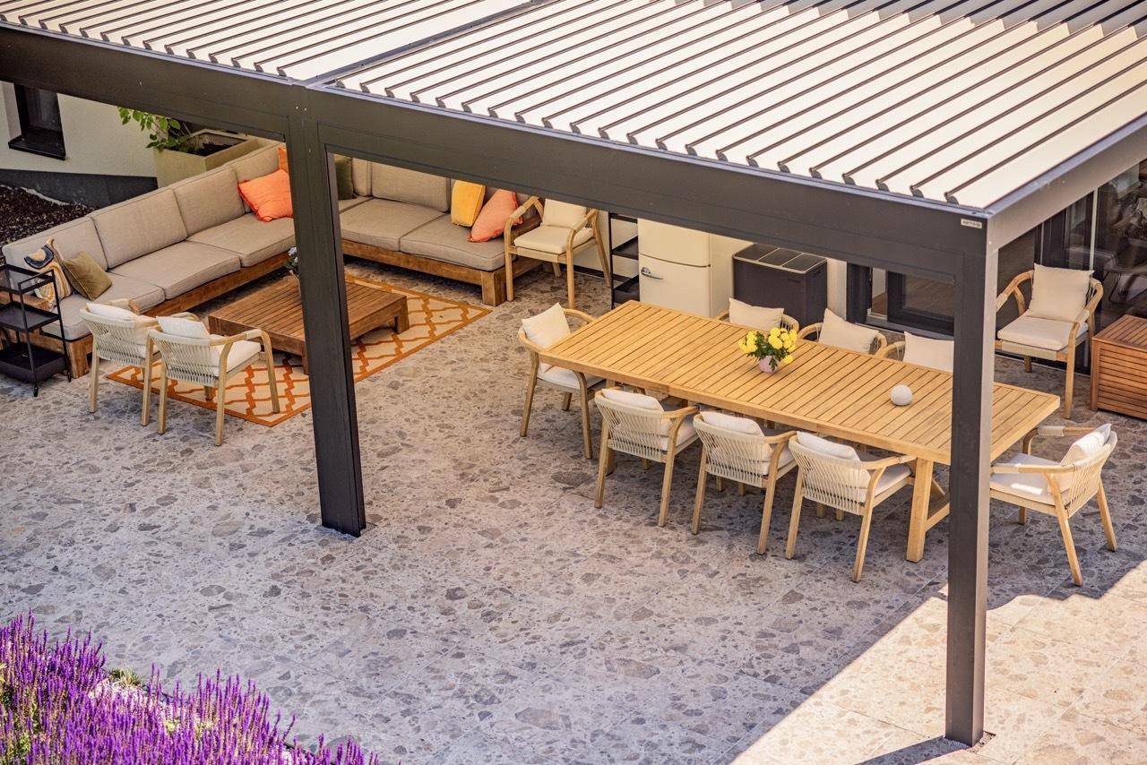 Detailansicht der überdachten Terrasse mit großem Esstisch und bequemen Lounge-Möbeln.