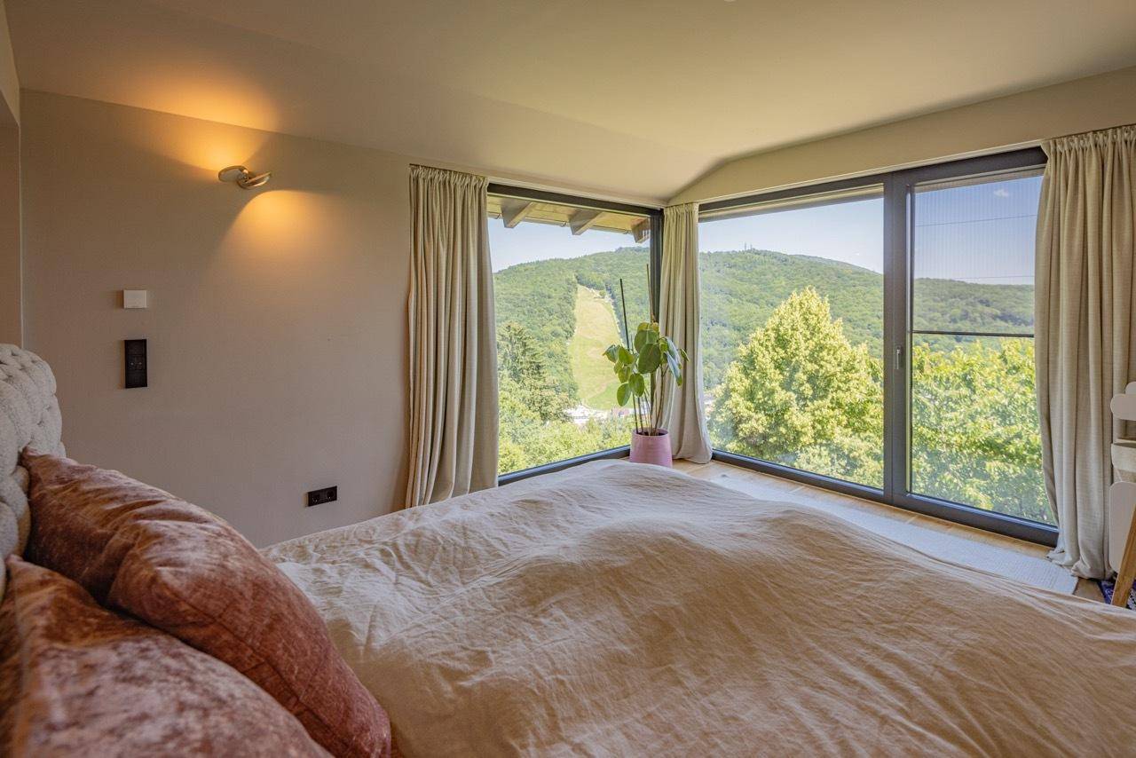 Schlafzimmer mit großem Bett und Panoramafenstern, die einen weiten Blick ins Grüne bieten.