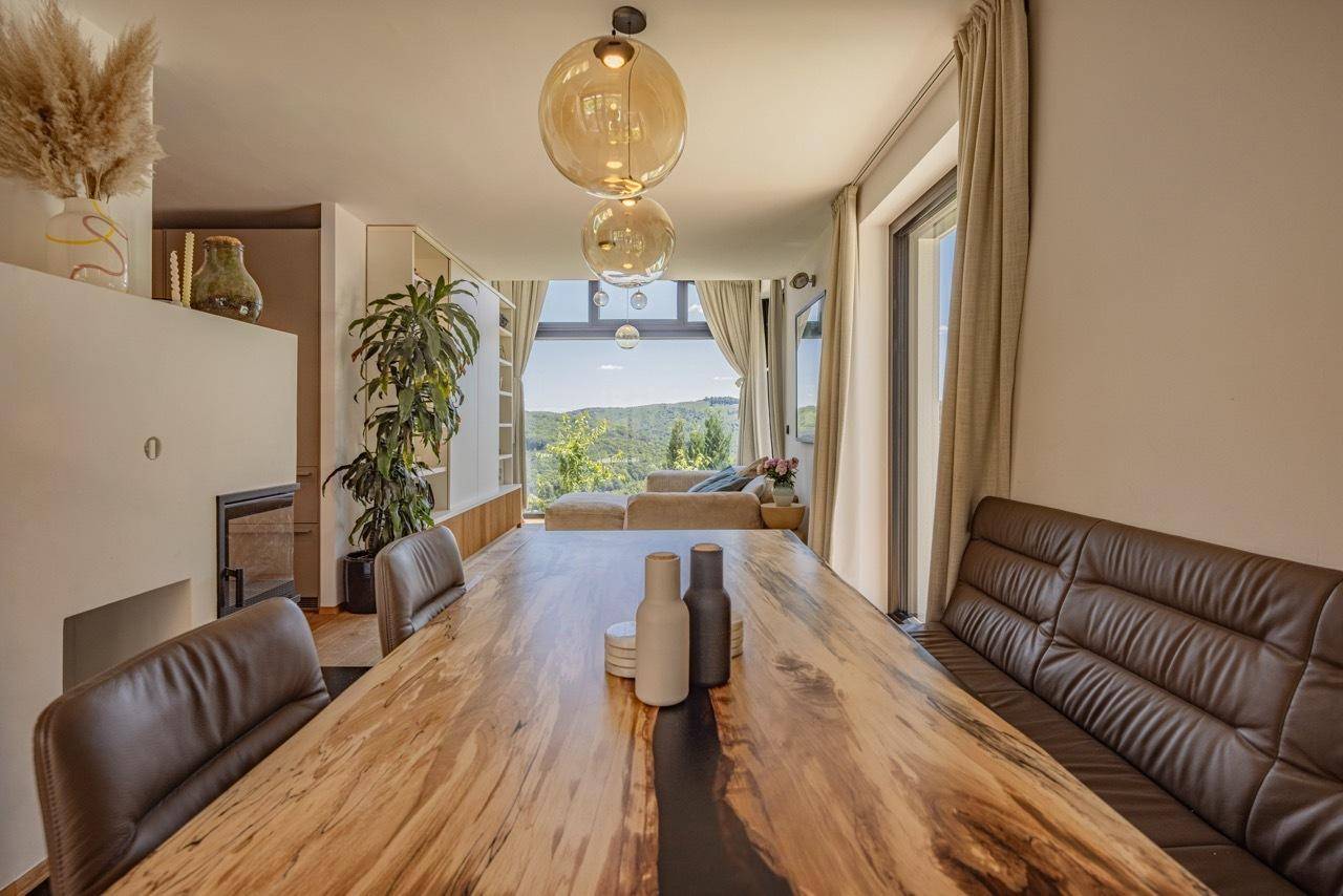 Essbereich mit großem Holztisch und Panoramablick auf die grüne Hügellandschaft.