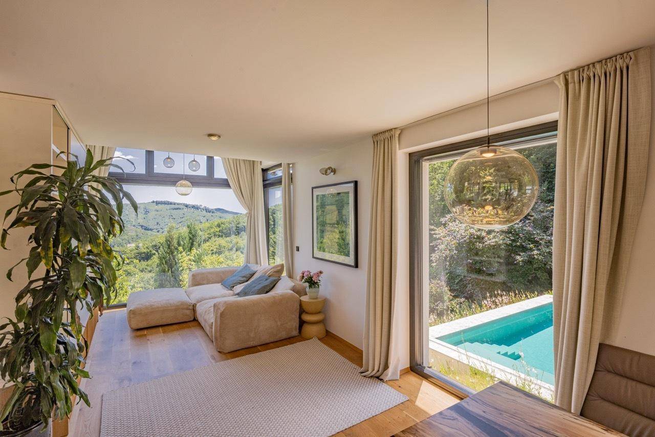 Gemütliches Wohnzimmer mit großen Fenstern, Blick auf den Pool und die Natur.