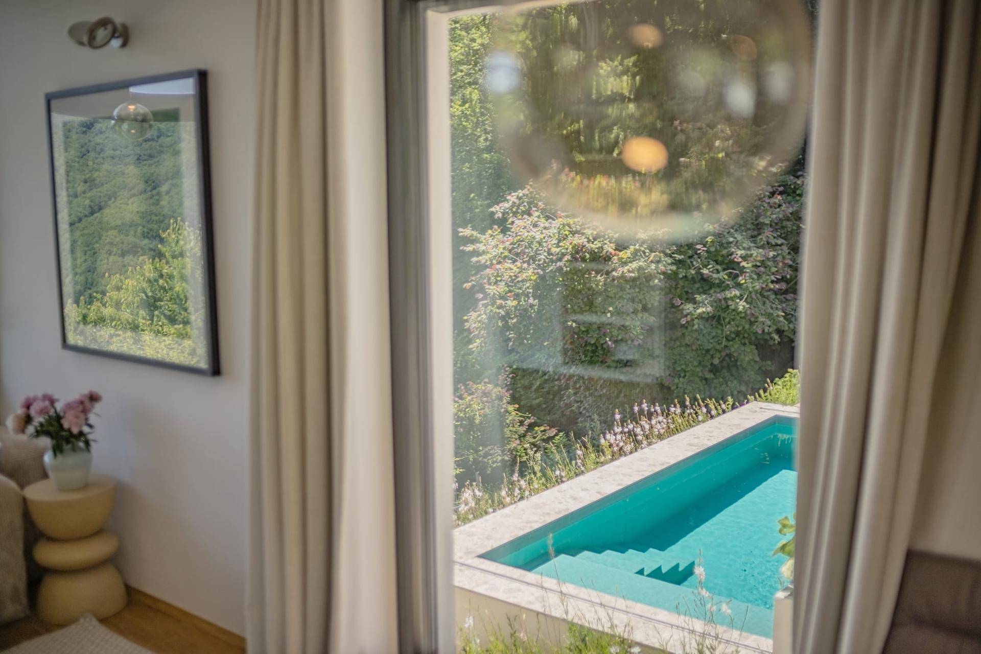 Blick aus dem Wohnzimmerfenster auf den privaten Pool und die üppige Vegetation.