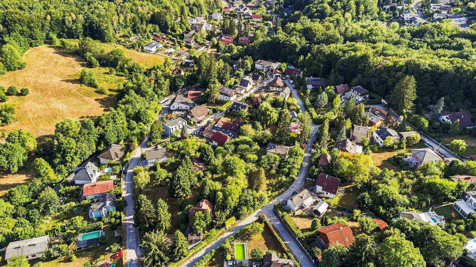 Weitläufiger Blick auf eine ländliche Siedlung, eingebettet in eine hügelige, waldreiche Landschaft.