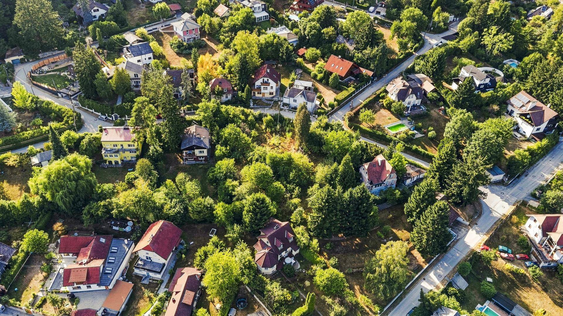 Panoramische Luftaufnahme einer ländlichen Siedlung, eingebettet in ein grünes Tal mit bewaldeten Hügeln unter blauem Himmel.