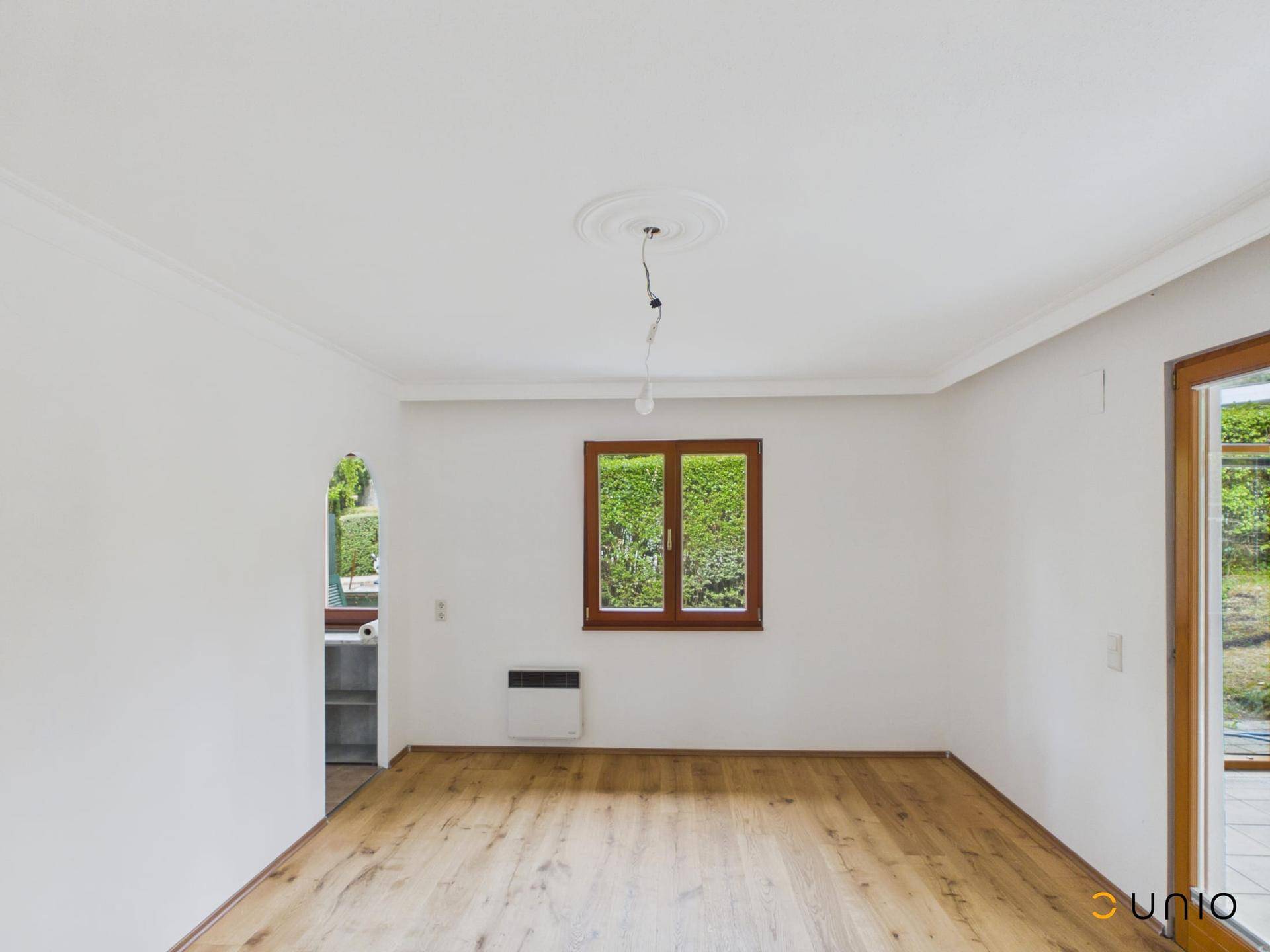Geräumiges Wohnzimmer mit Holzboden, weißen Wänden und Bogenzugang zur Küche.