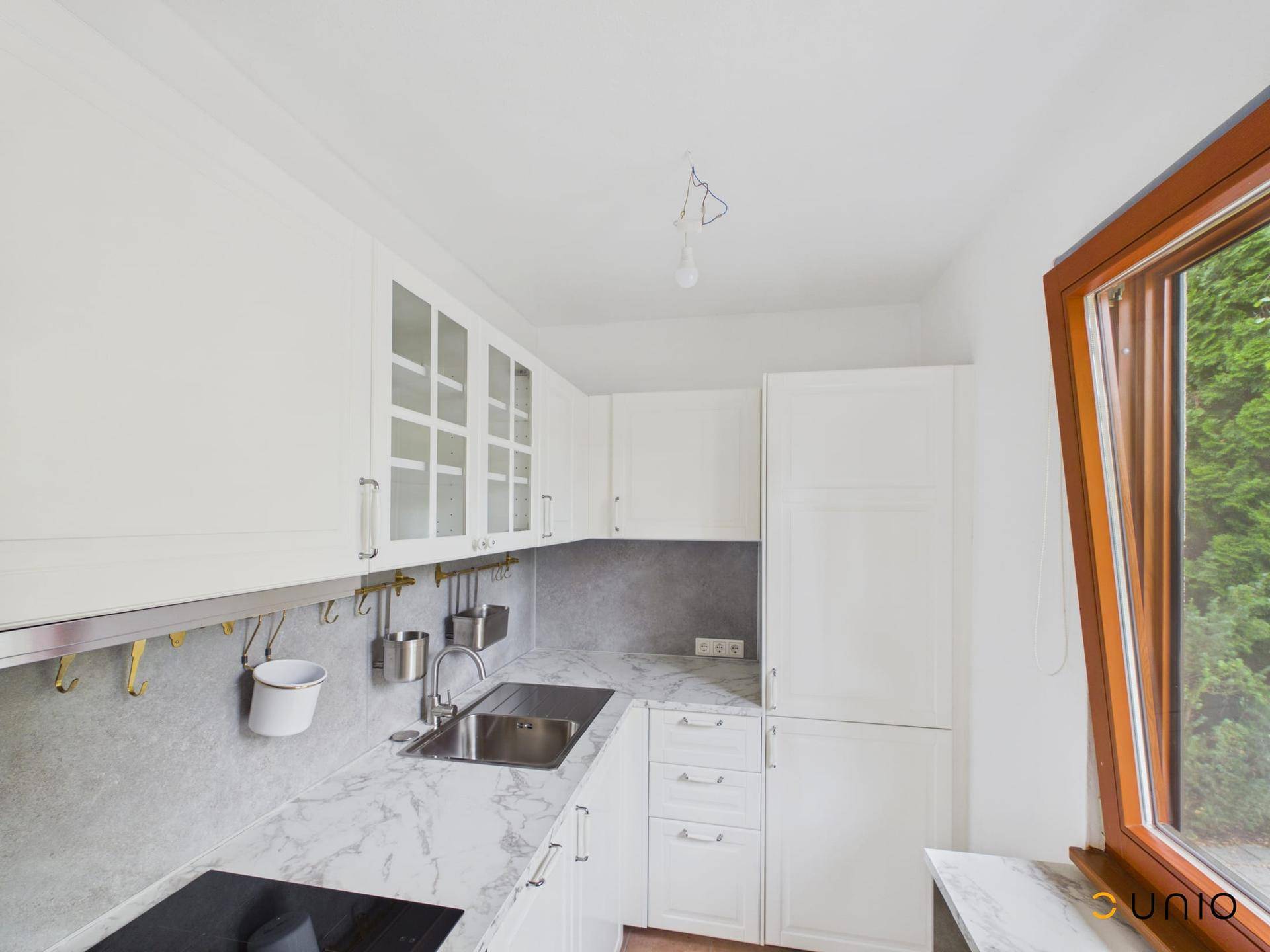 Moderne weiße Küche mit Marmor-Arbeitsplatte, Induktionskochfeld und Fenster zum Garten.