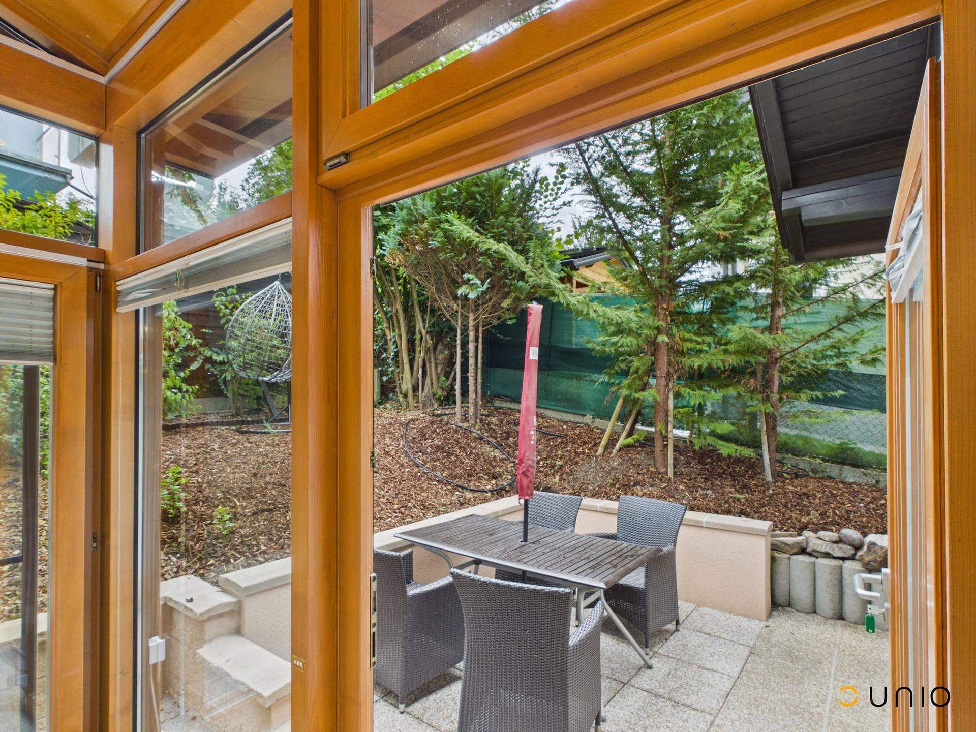 Gemütliche Terrasse mit Esstisch und Stühlen, umgeben von Bäumen und Sträuchern.