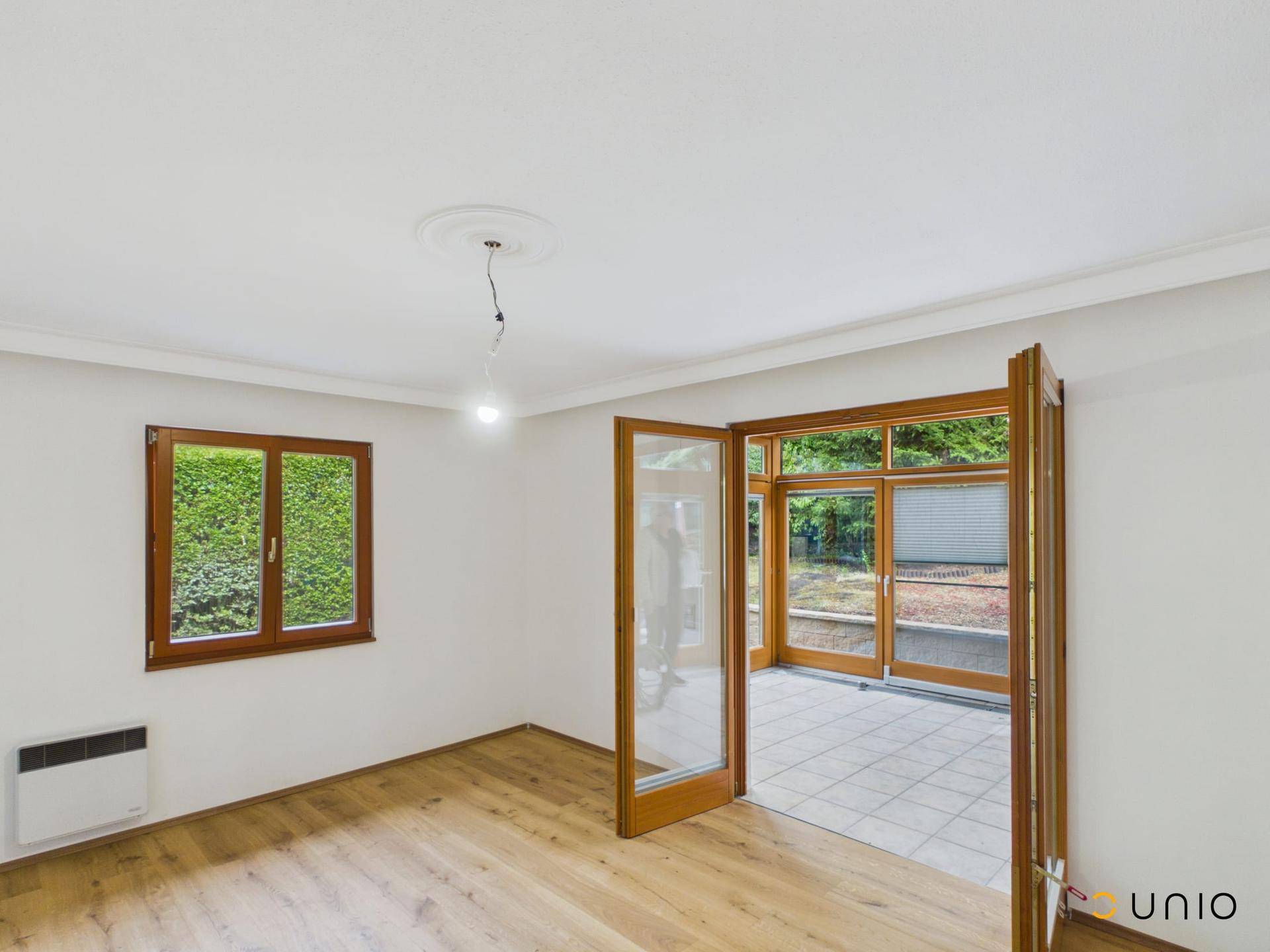Helles Wohnzimmer mit Holzboden, weißen Wänden und geöffneten Türen zum Wintergarten.