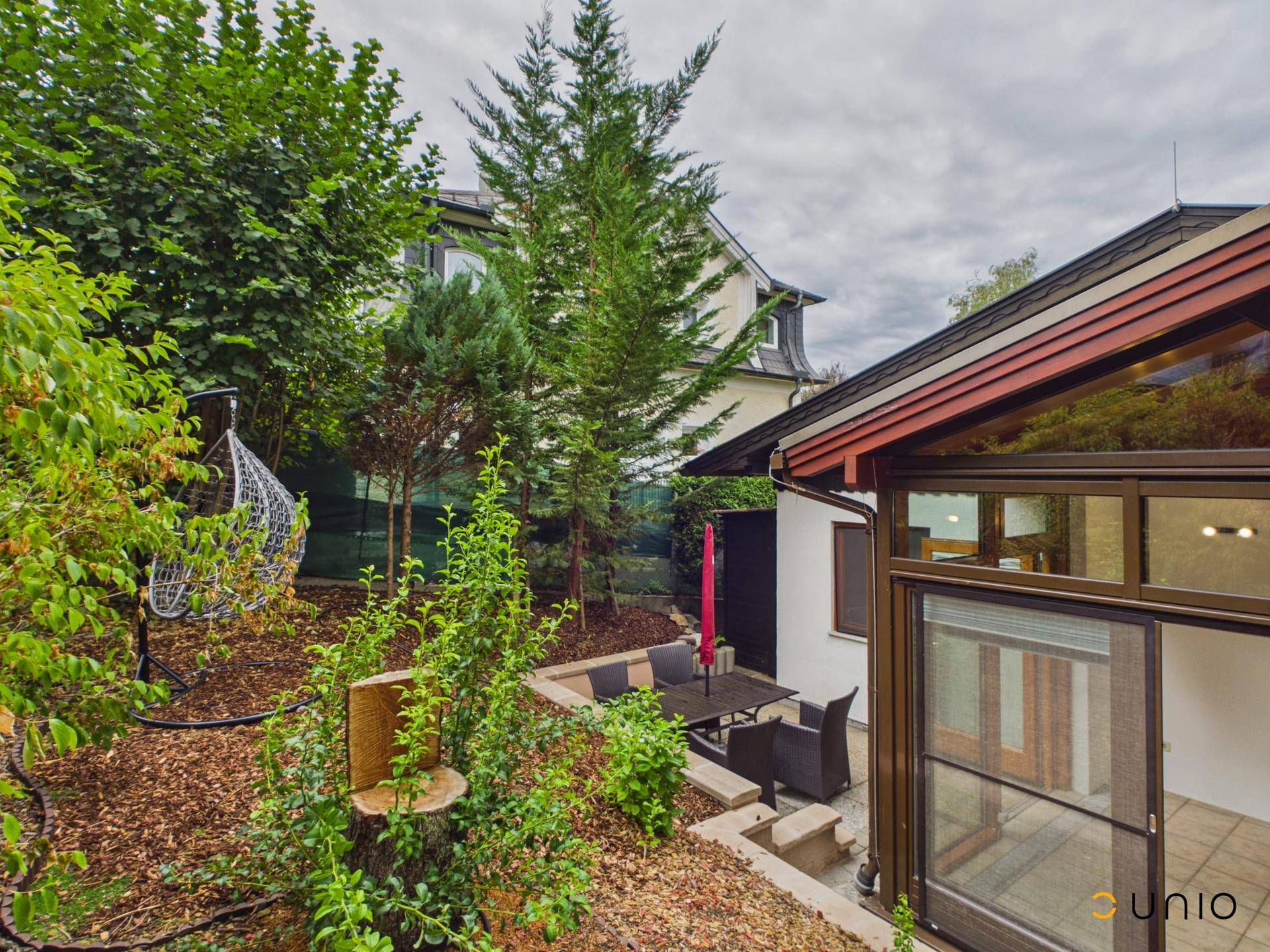 Außenansicht des Hauses mit Wintergarten, Terrasse und üppigem Grün im Gartenbereich.