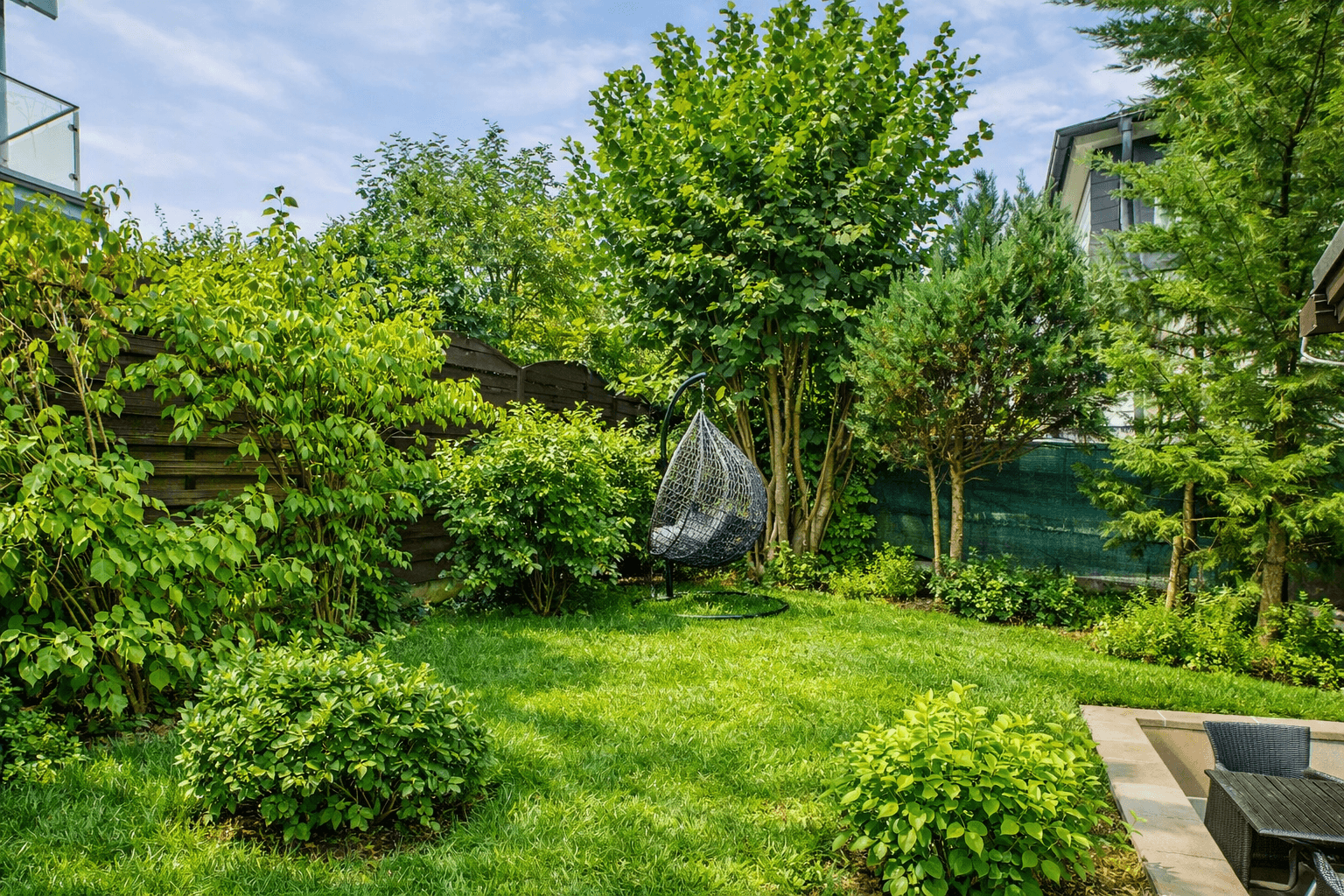 Gepflegter Garten mit Rasenfläche, Sträuchern und einem Hängesessel im Grünen.