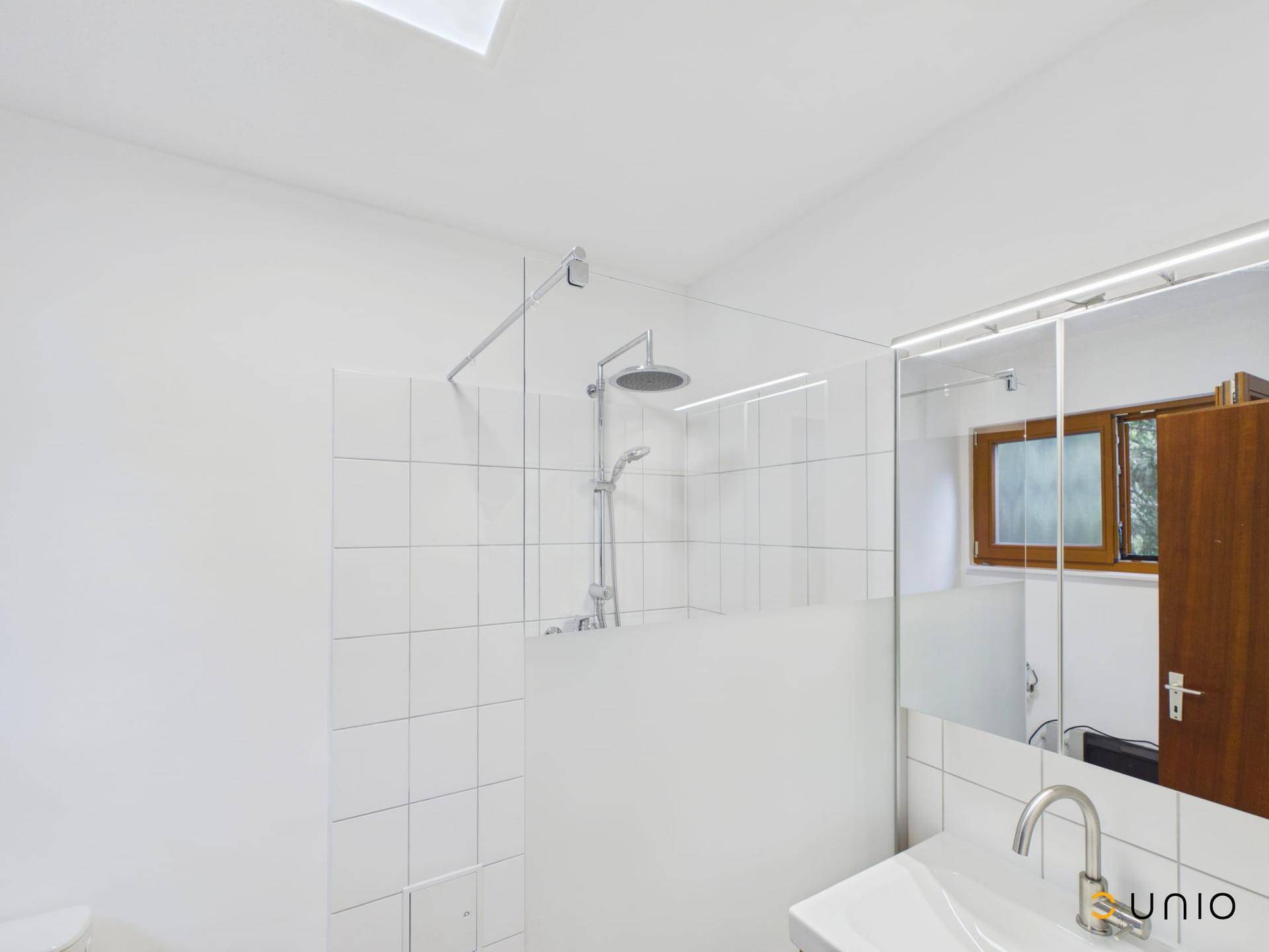 Modernes Badezimmer mit weiß gefliestem Duschbereich, Einzelwaschbecken und Spiegelschrank.