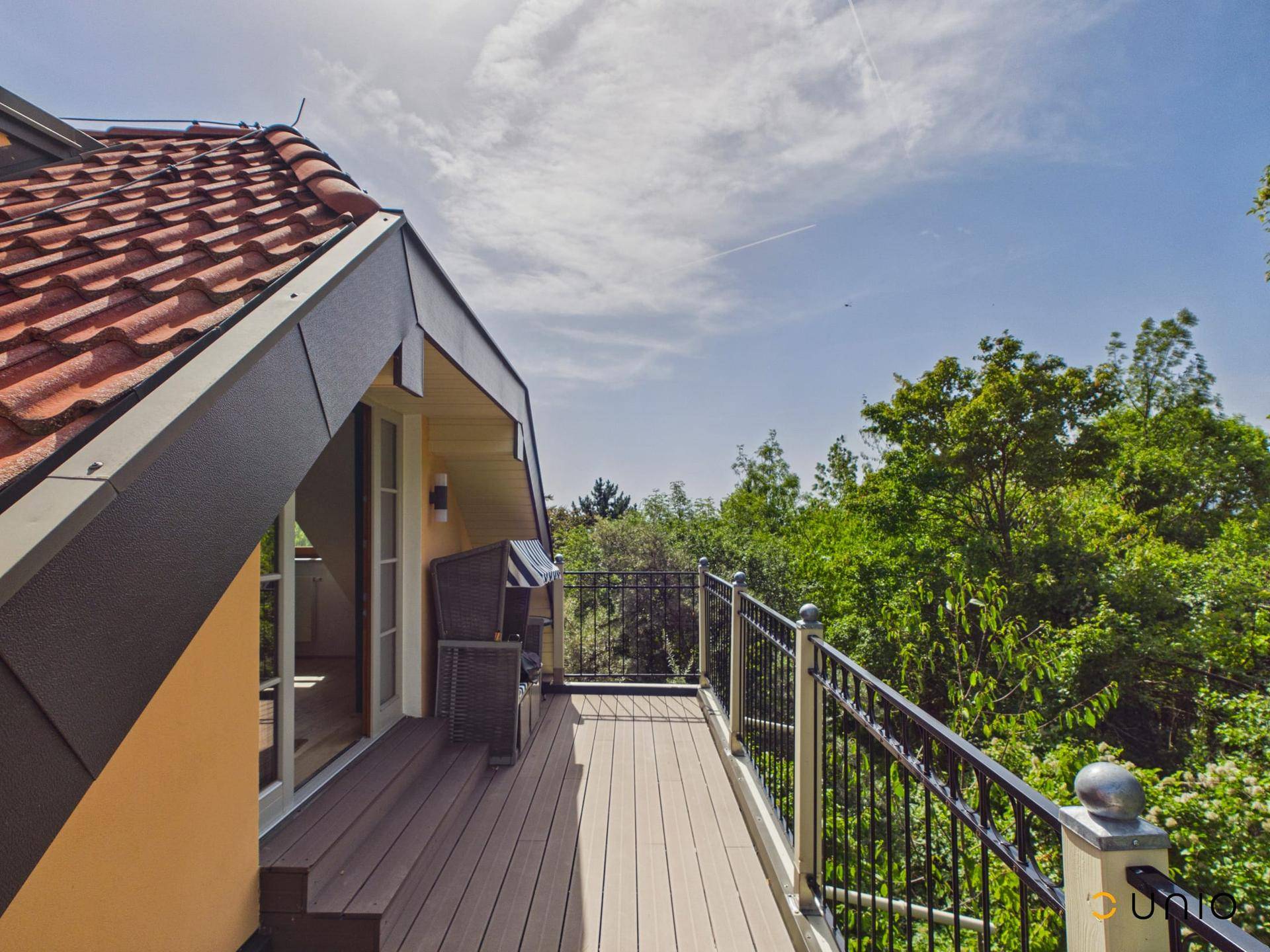 Geräumiger Balkon mit Holzdeck und Metallgeländer, bietet einen weiten Blick ins Grüne.