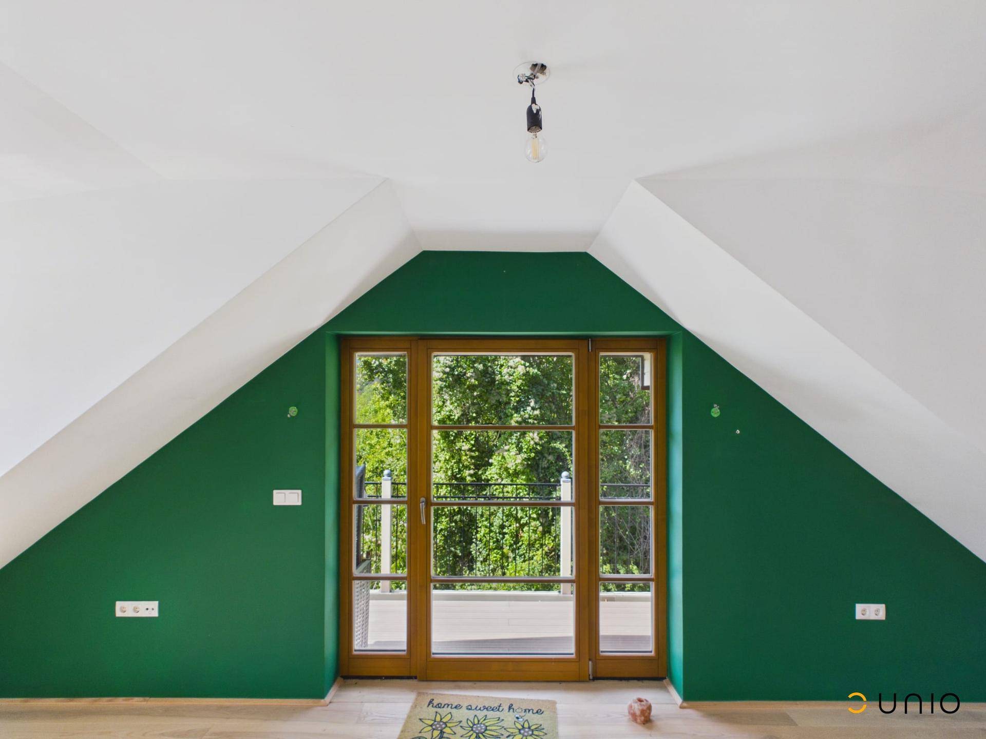 Helles Dachzimmer mit grüner Akzentwand und Zugang zu einem französischen Balkon.