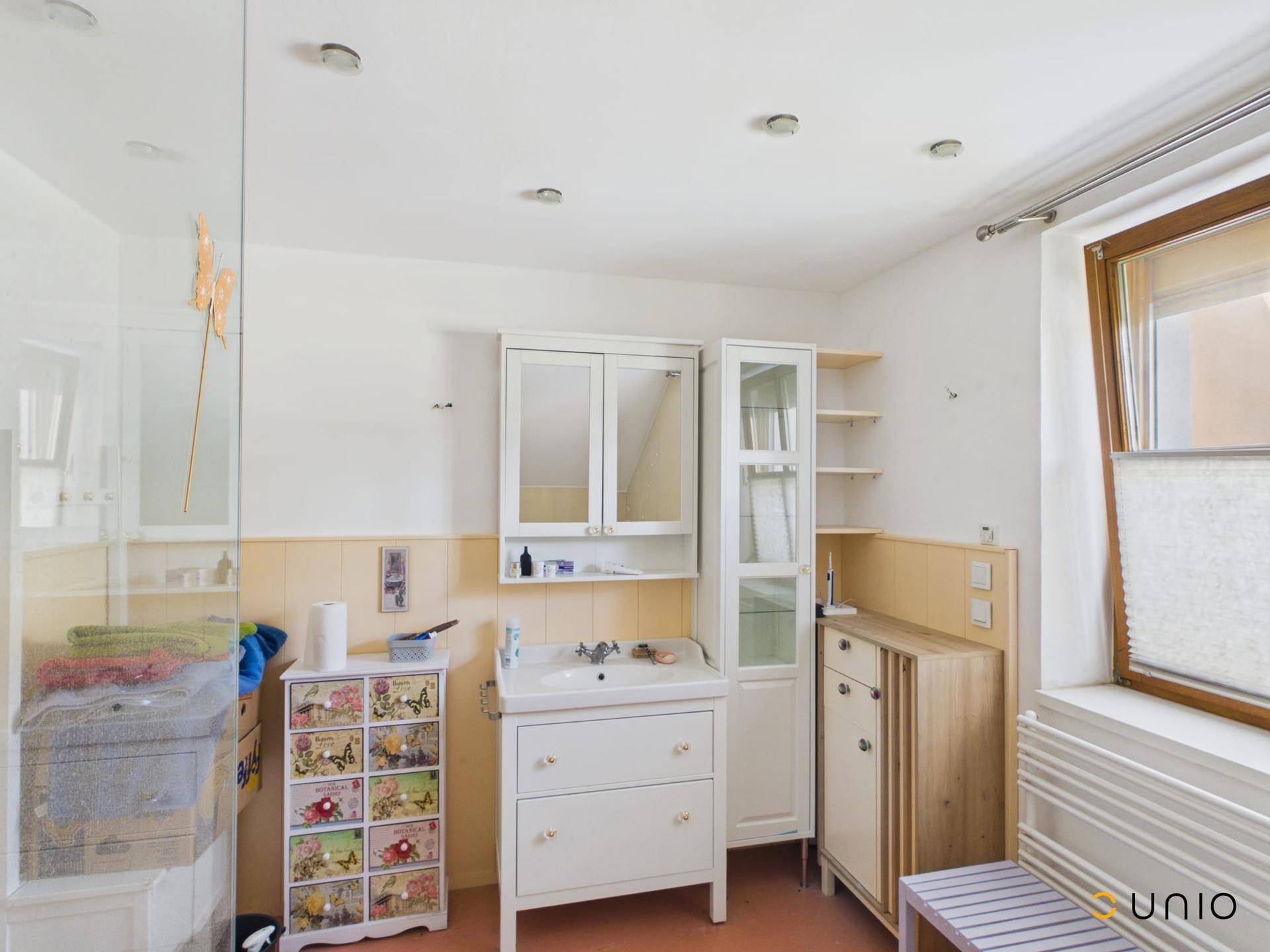 Helles Badezimmer mit Einzelwaschbecken, Spiegelschrank und Fenster, im Vintage-Stil eingerichtet.