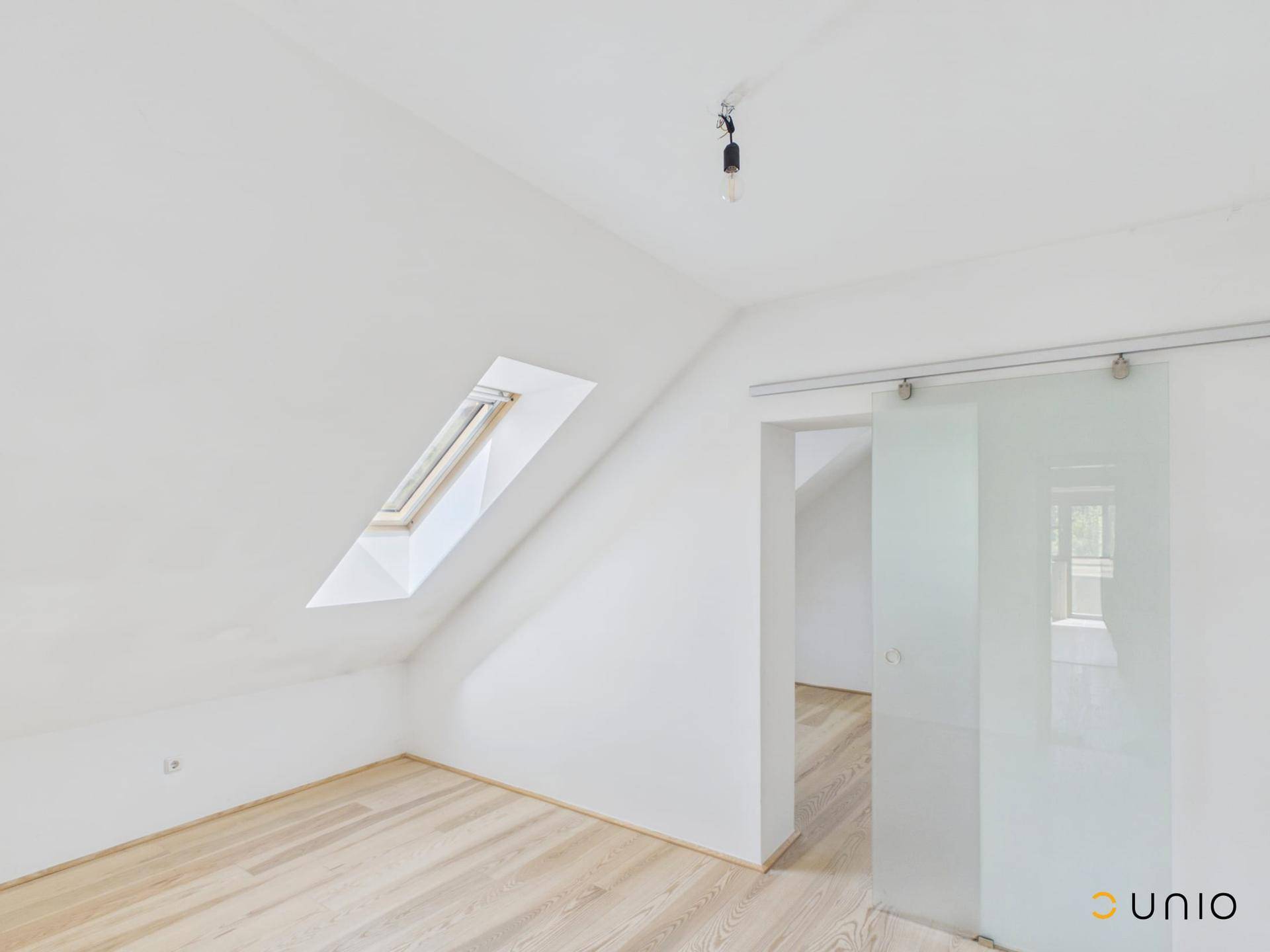 Helles Dachzimmer mit Holzfußboden, Schiebetür aus Glas und einem Dachfenster für Tageslicht.
