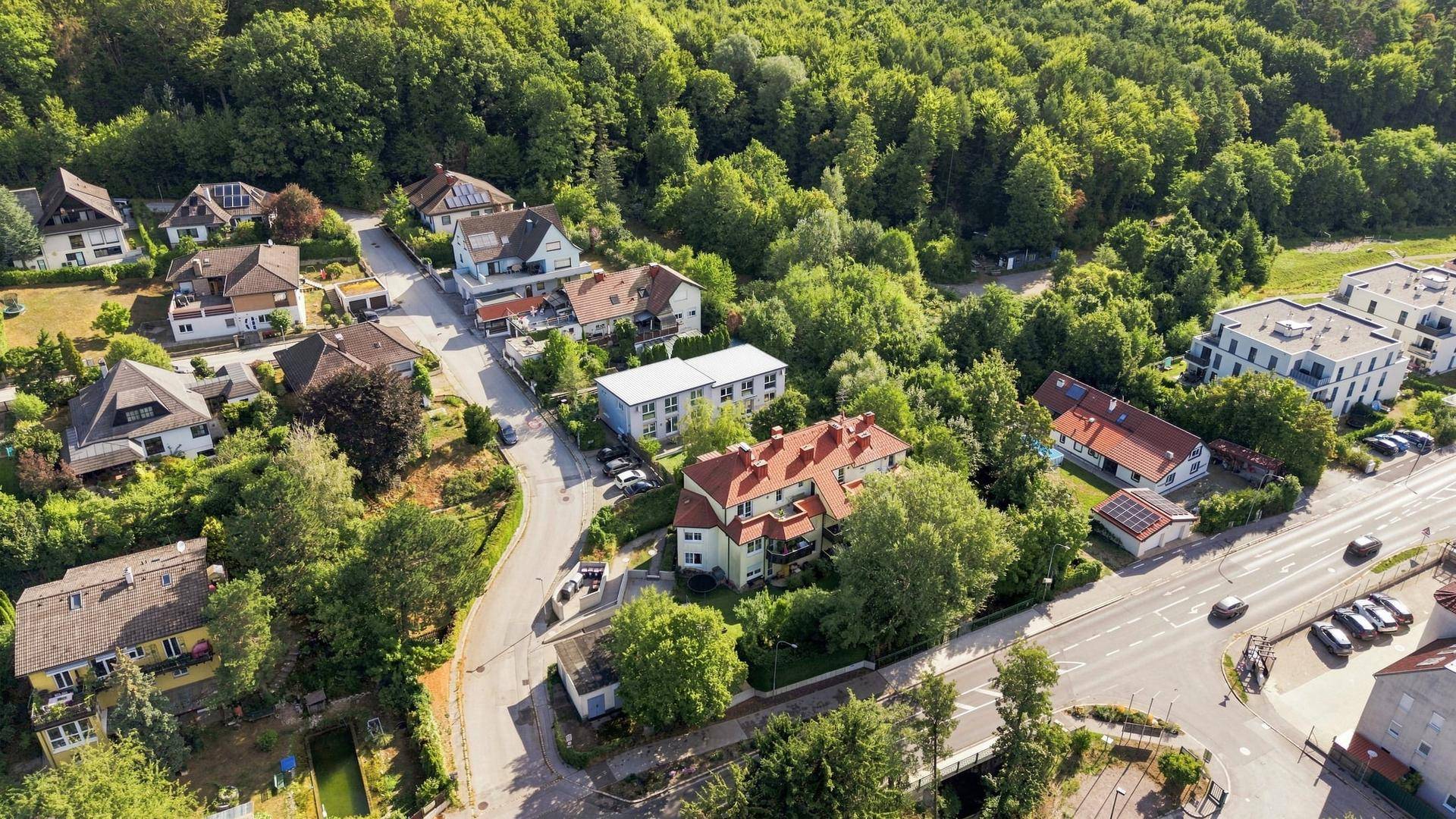Luftaufnahme einer Wohnsiedlung am Waldrand mit verschiedenen Gebäudetypen und Straßen.