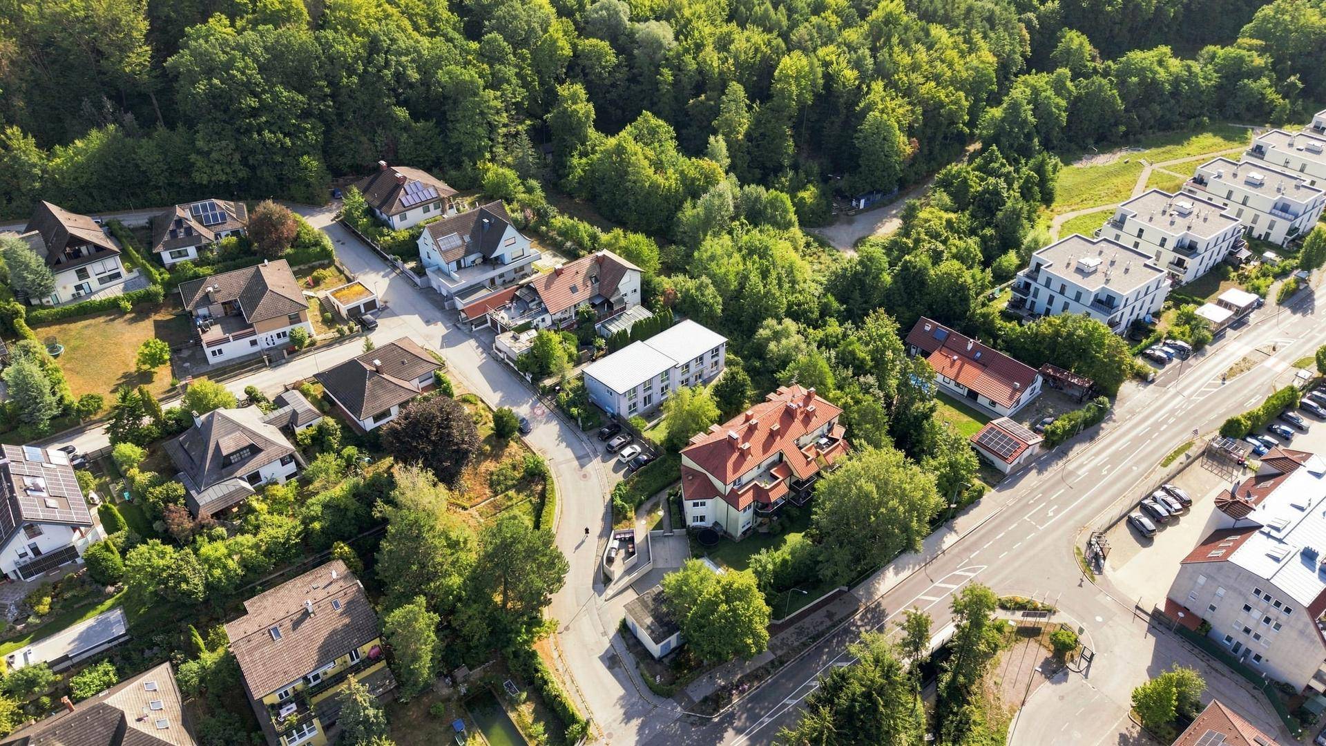 Luftaufnahme einer weitläufigen Wohnsiedlung mit viel Baumbestand und angrenzenden Waldgebieten.