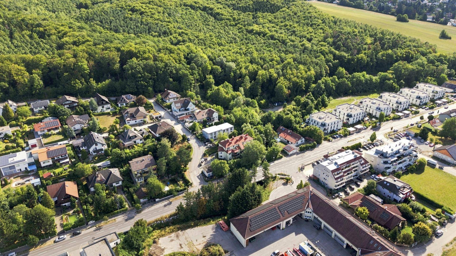 Panoramablick aus der Luft auf eine Wohnsiedlung am Waldrand mit Feldern im Hintergrund.