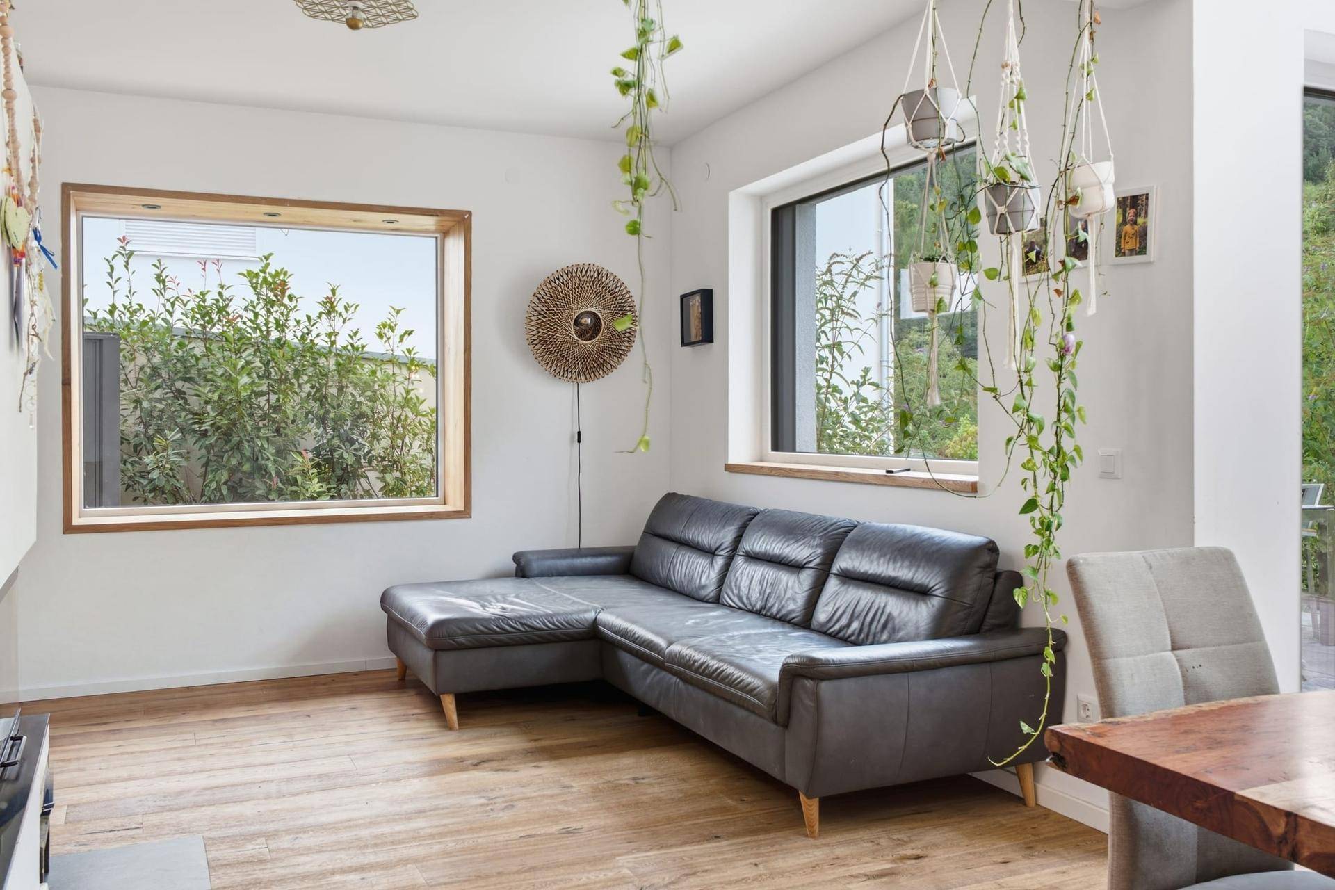 Gemütliches Wohnzimmer mit Ledersofa, Holzboden und Blick ins Grüne.