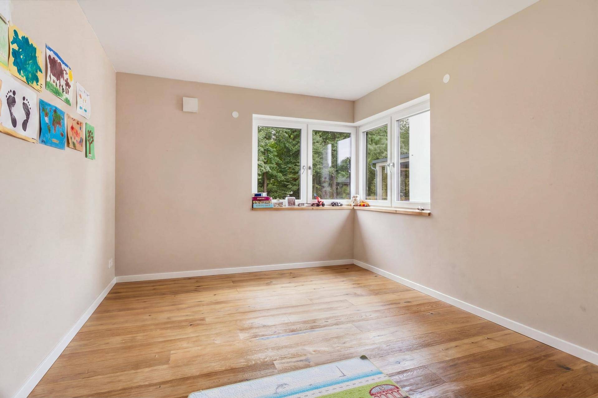 Kinderzimmer mit Holzboden, großen Fenstern und Blick ins Grüne.