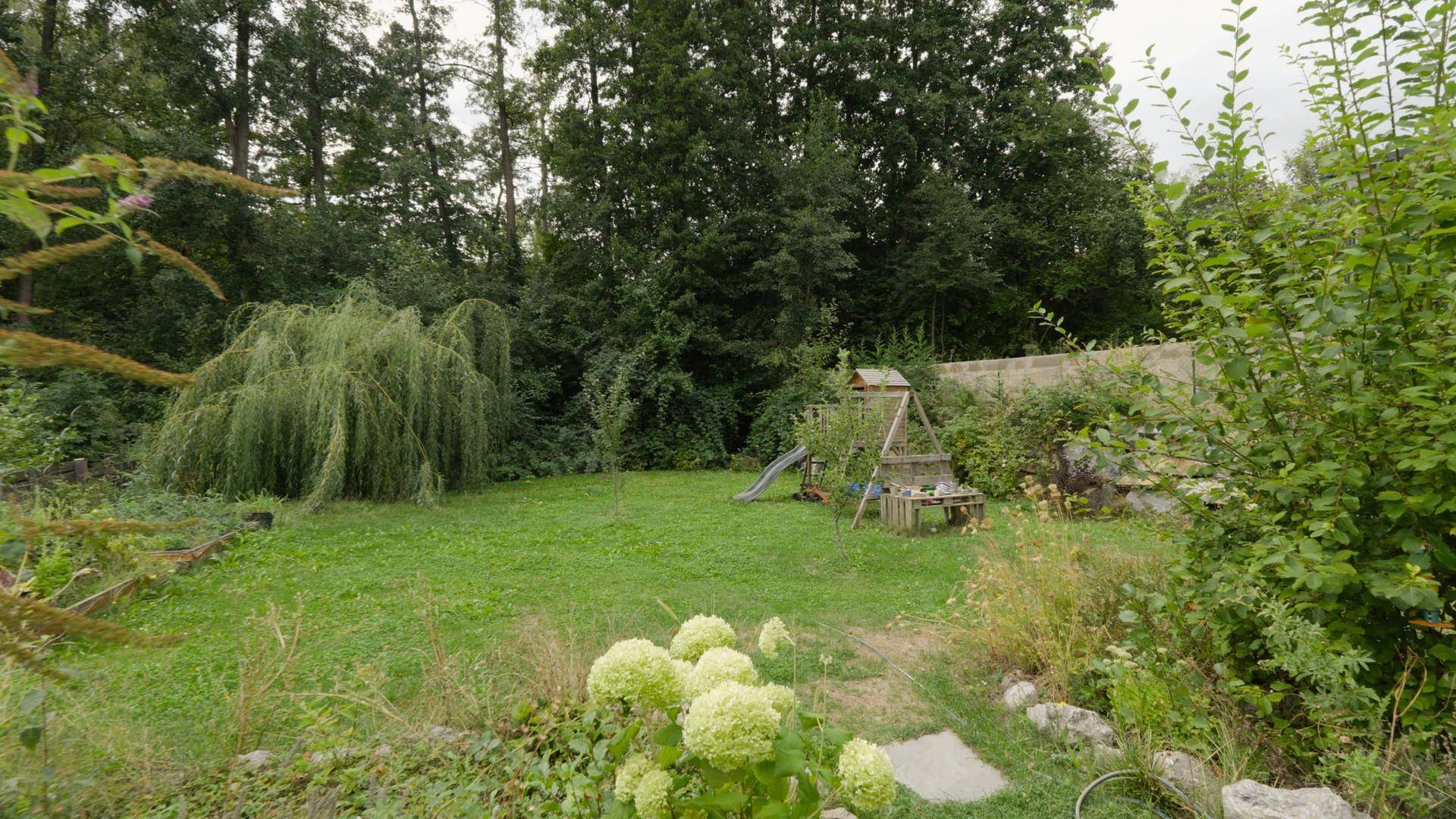 Großer grüner Garten mit Rasenfläche, Bäumen und Kinderspielgerät.